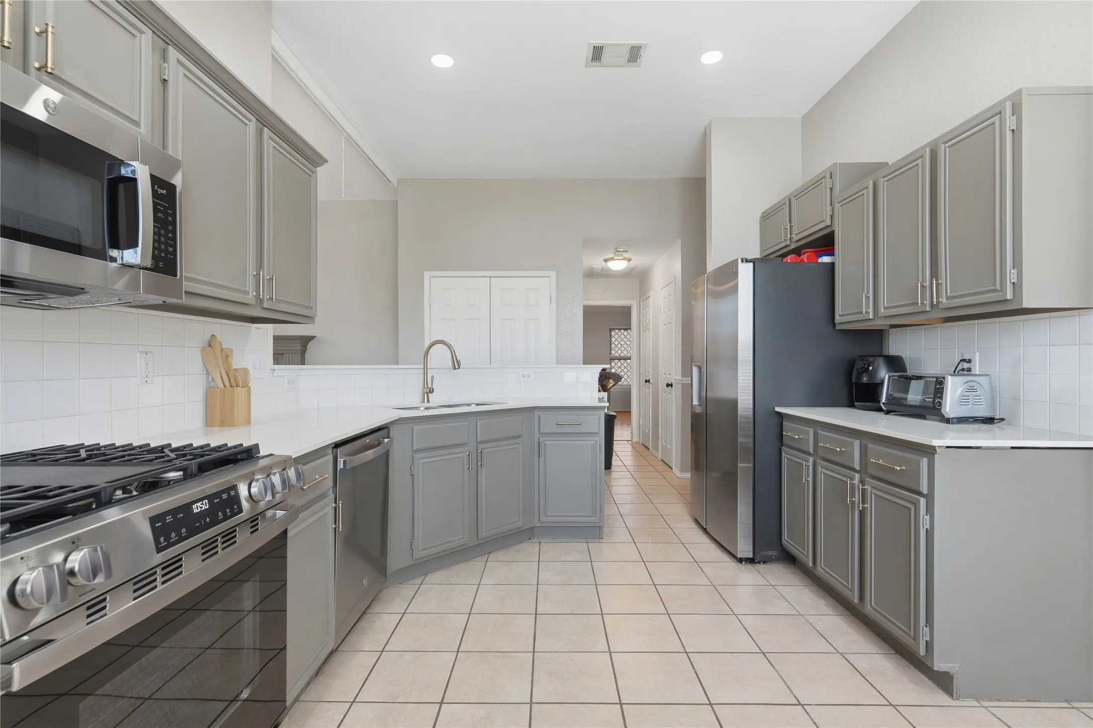 Kitchen featuring stainless steel appliances, white subway tile backsplash, light grey cabinetry, quartz countertops, and tile flooring