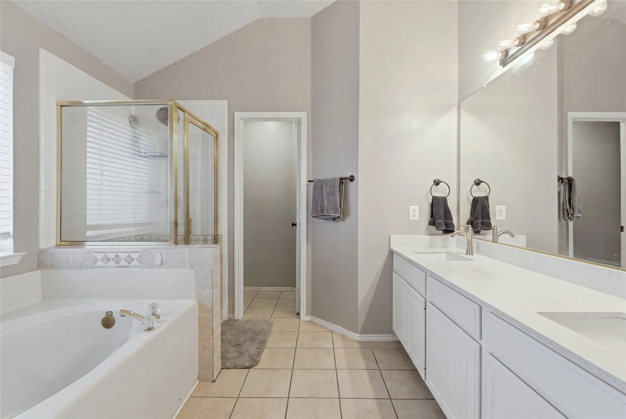 Dual vanity with white cabinetry and integrated sinks, a built-in tub, and a shower with a gold-finish frame