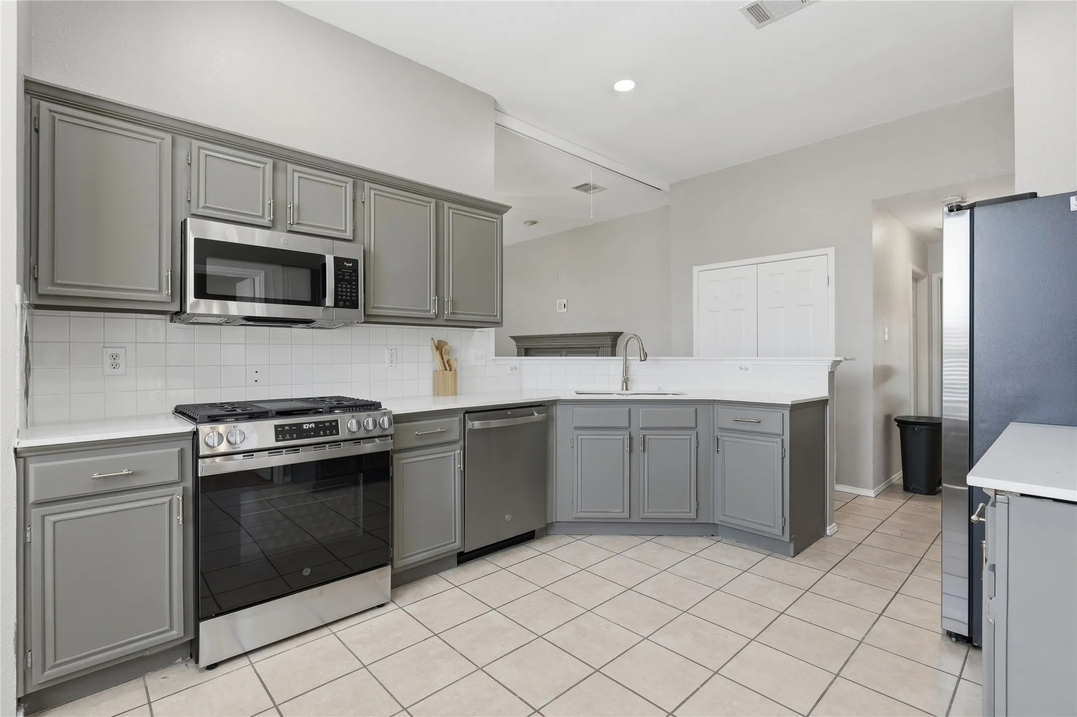Kitchen featuring gray cabinetry, quartz countertops, tile flooring, stainless steel appliances, and a white tile backsplash