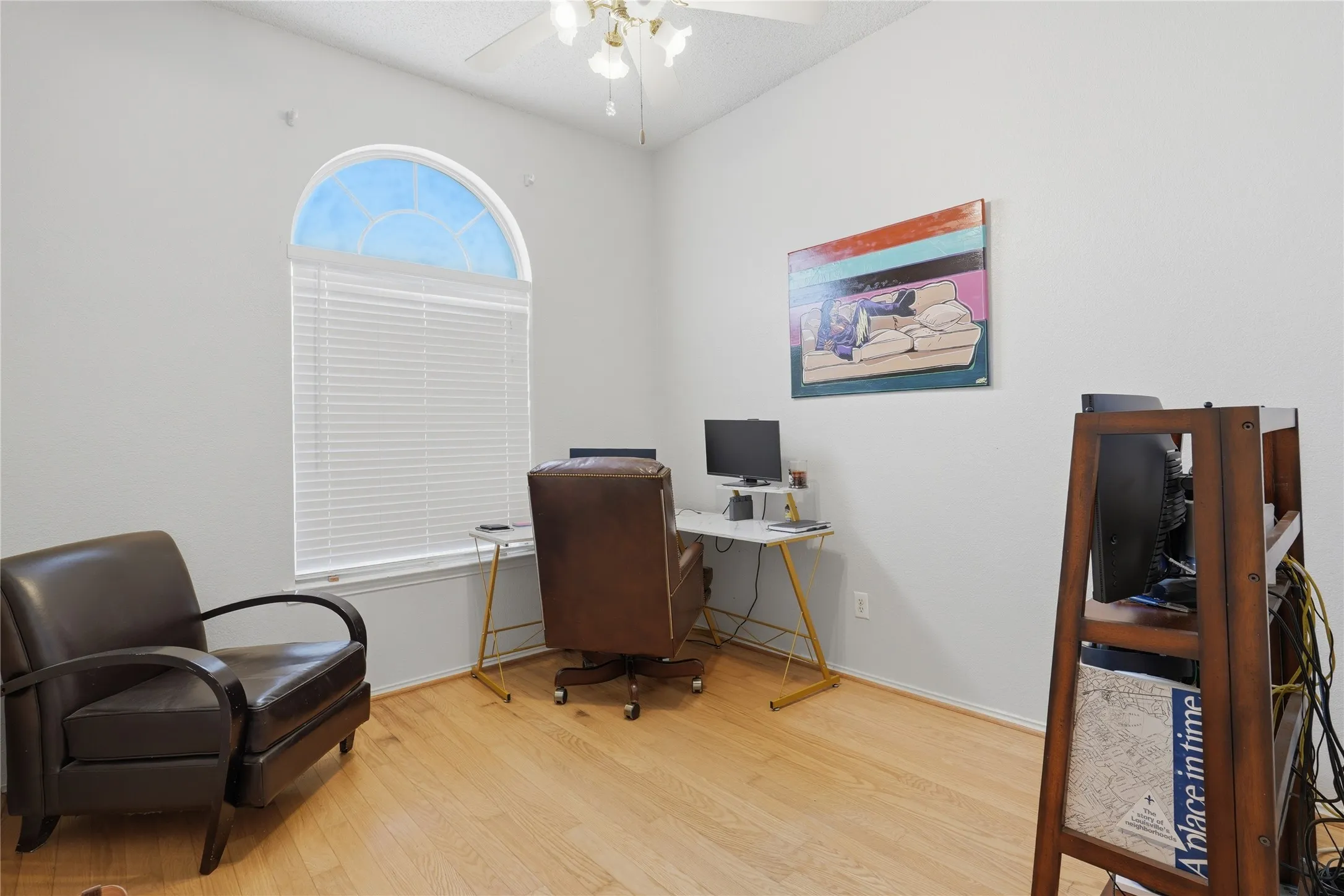 Arched window with blinds, vaulted ceiling, ceiling fan with light fixture, light wood-finish flooring, and neutral wall paint