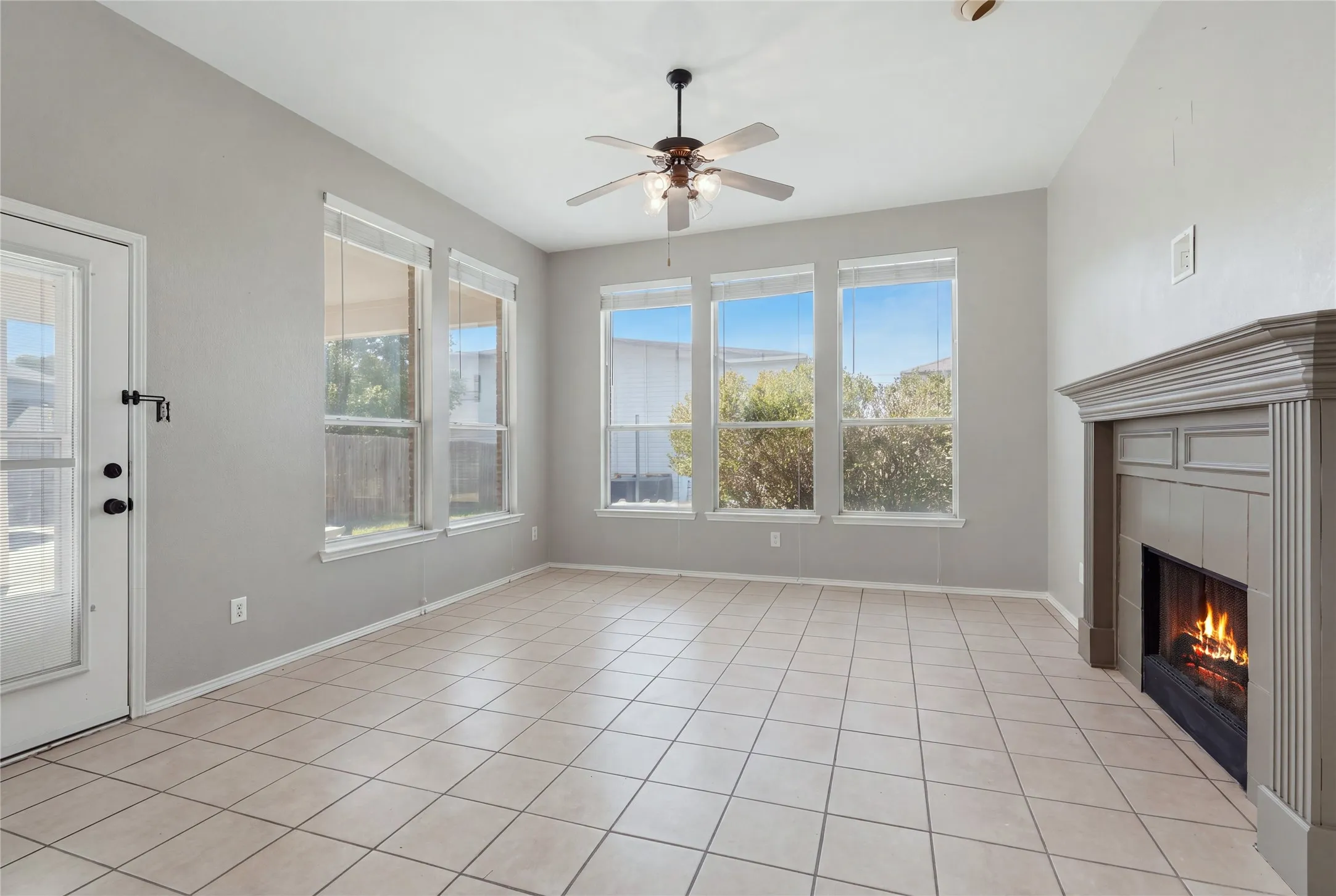 Tile flooring, a ceiling fan, multiple windows, a fireplace with a mantel, and a glass-paneled door