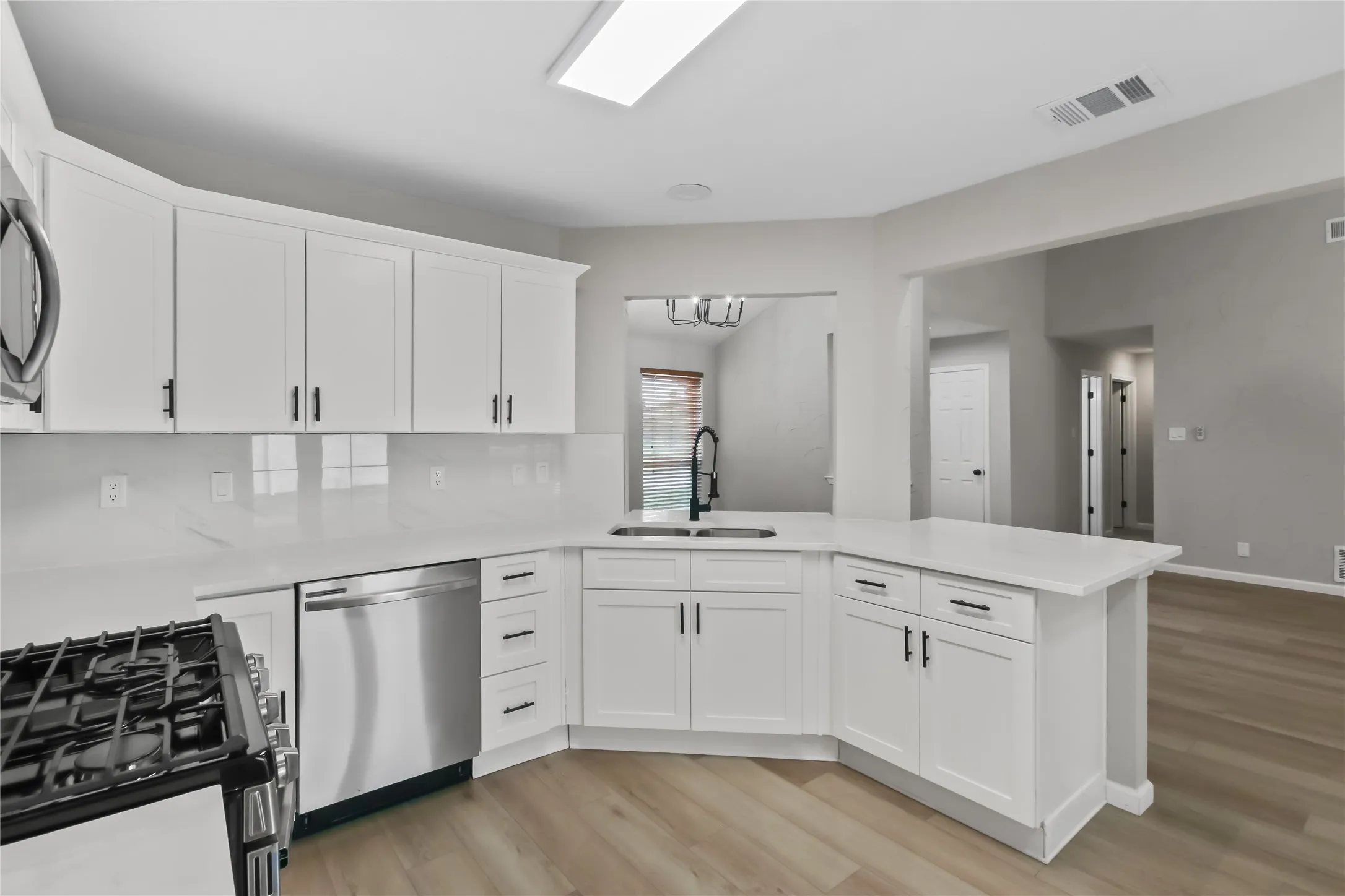 White cabinetry with matte black hardware, stainless steel dishwasher, wood-finish flooring, and solid surface countertops