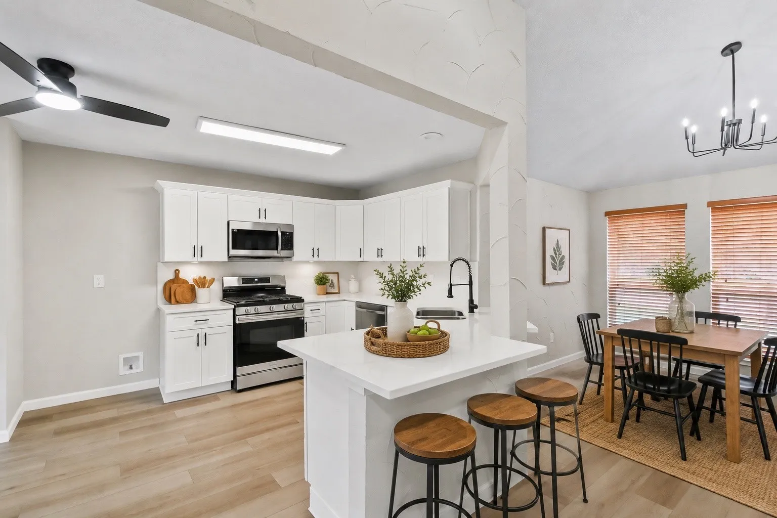 Modern kitchen and dining area featuring white cabinetry with stainless steel appliances, a large quartz-topped island with seating for three, wood-finish flooring throughout, and a pendant light fixture above the island