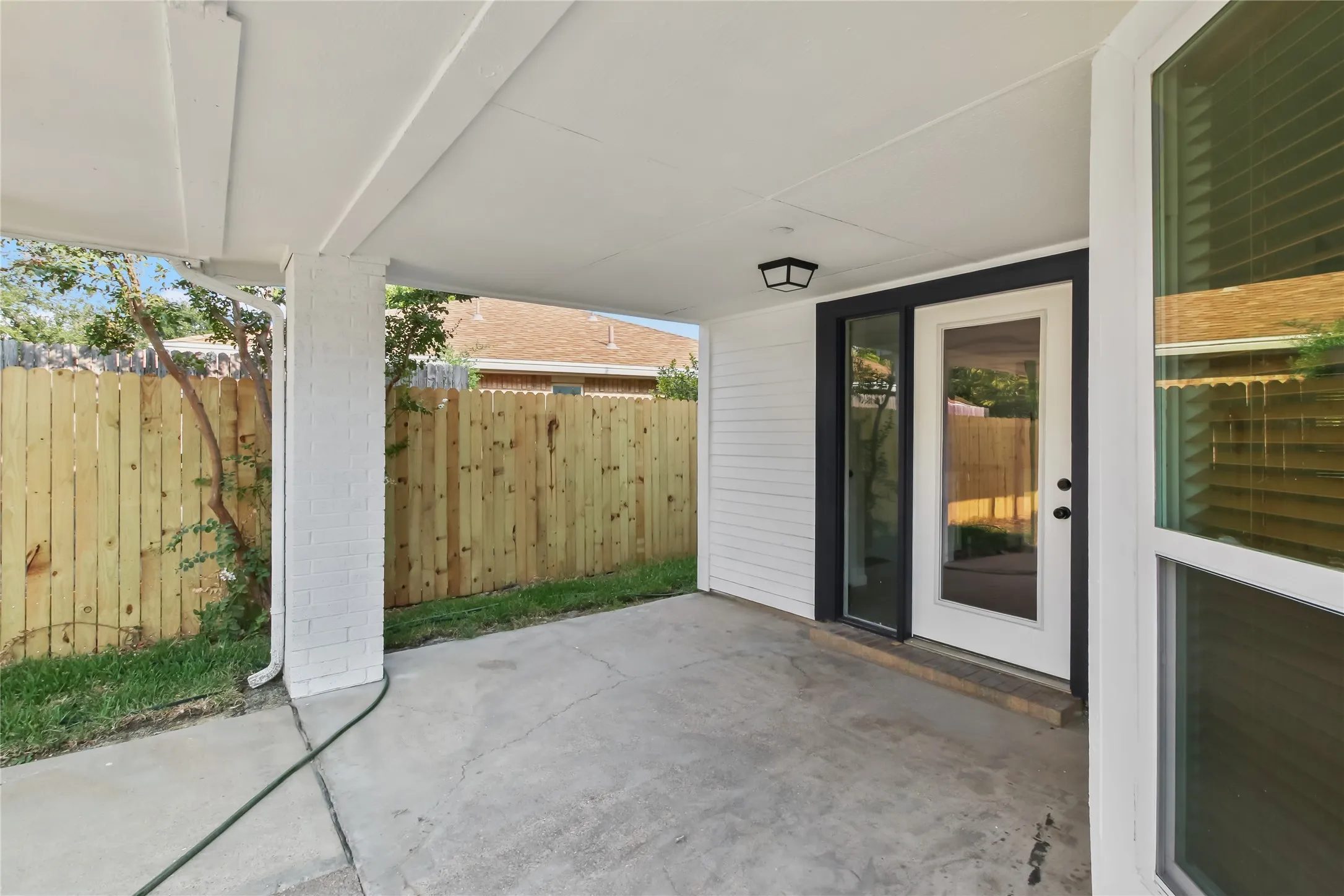 Covered patio with concrete flooring and white beam ceiling, opening to a fenced backyard with wood privacy fencing
