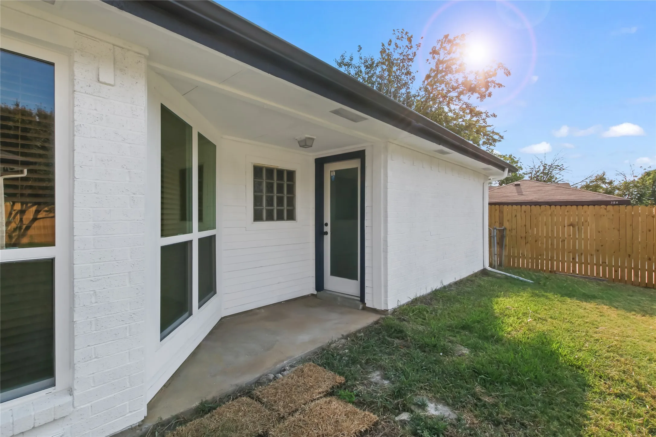 Covered patio area with a glass panel door, multiple large windows, and a privacy fence