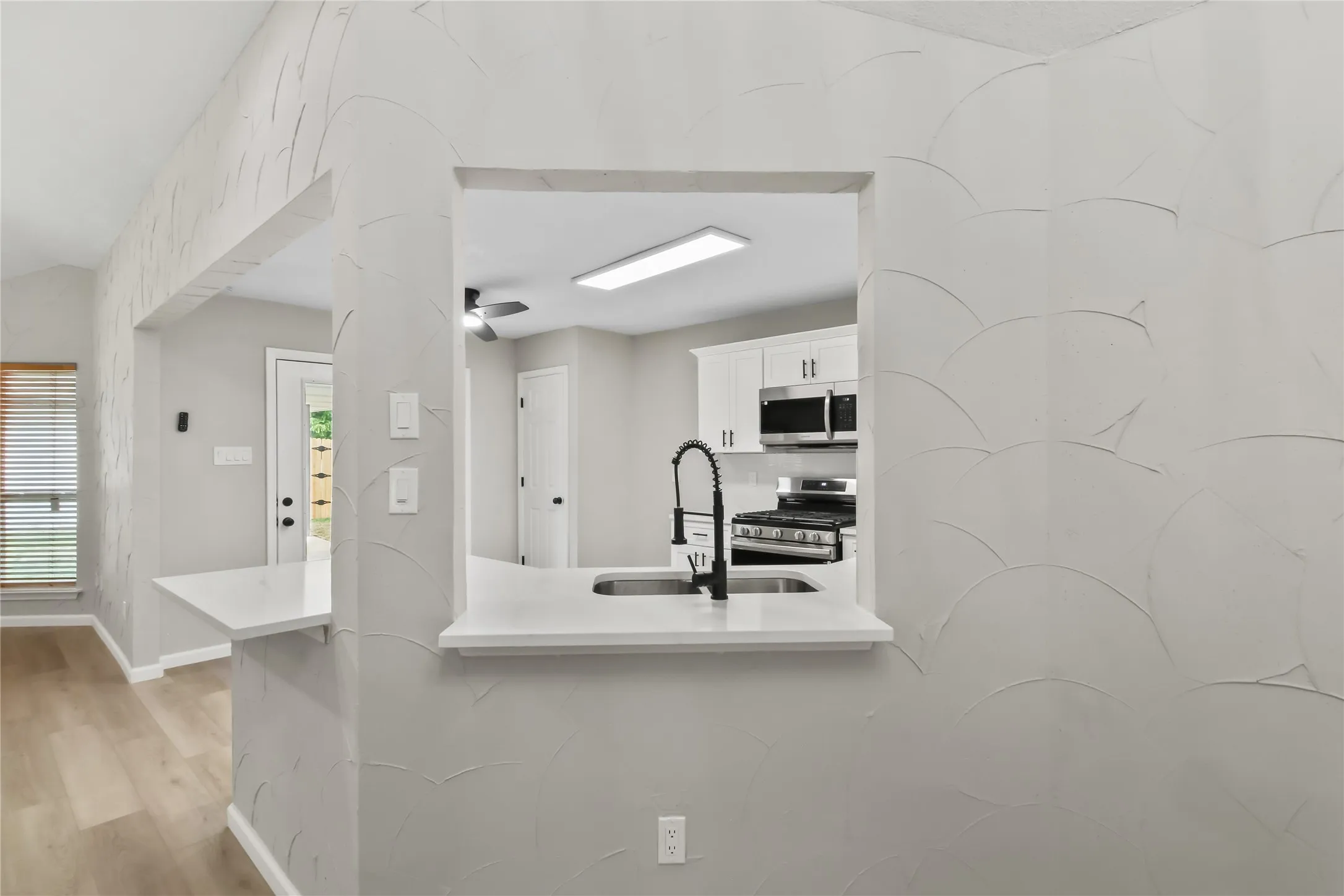 Modern kitchen featuring stainless steel appliances, a pull-down faucet with matte black finish, and a pass-through window opening to the adjacent living space