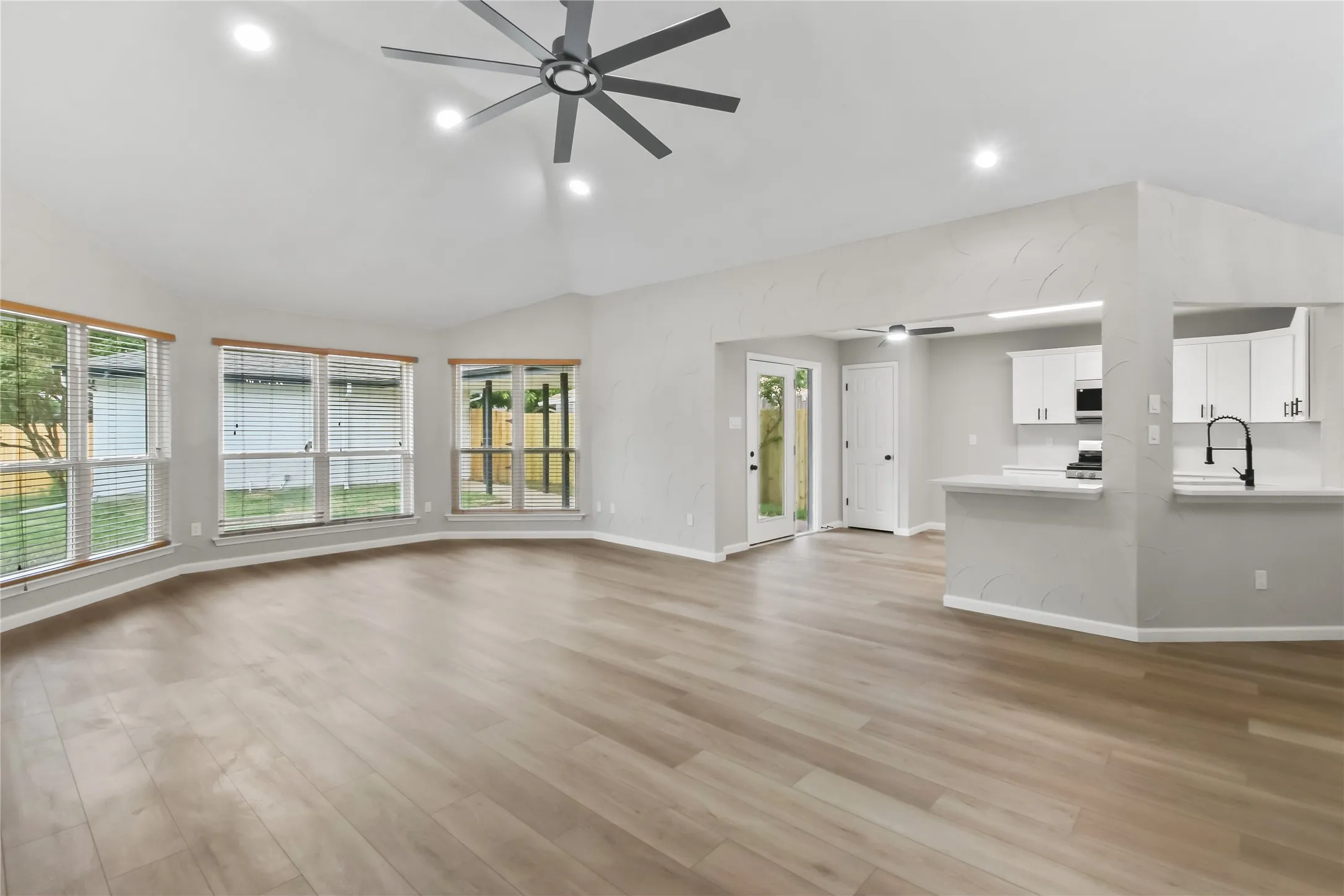 Vaulted ceilings with recessed lighting and a ceiling fan, wood-finish flooring, a kitchen pass-through, white cabinetry, and a modern black faucet