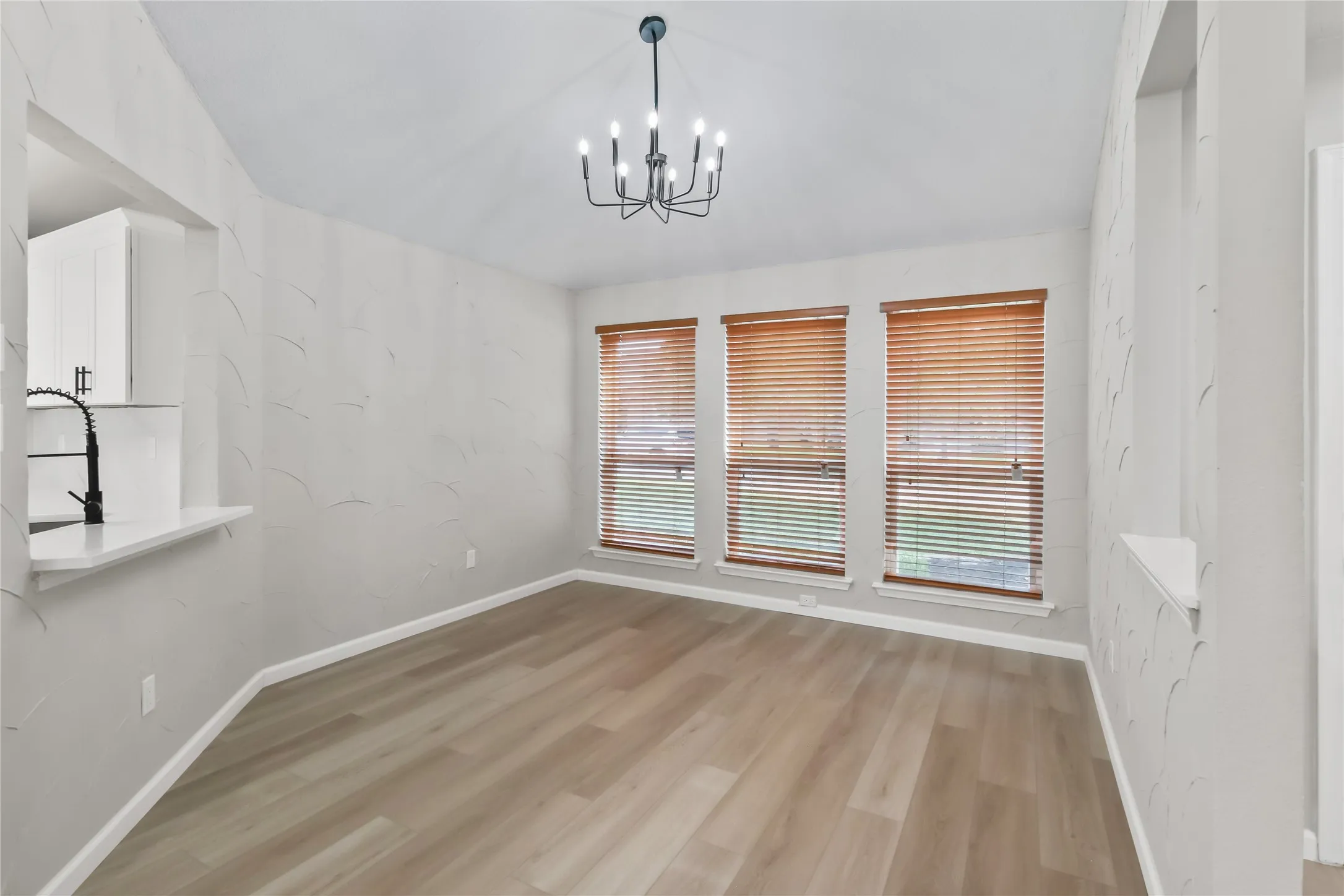 Bright corner room showcasing gleaming wood-finish flooring, triple casement windows with wood-grain blinds, and crisp white walls
