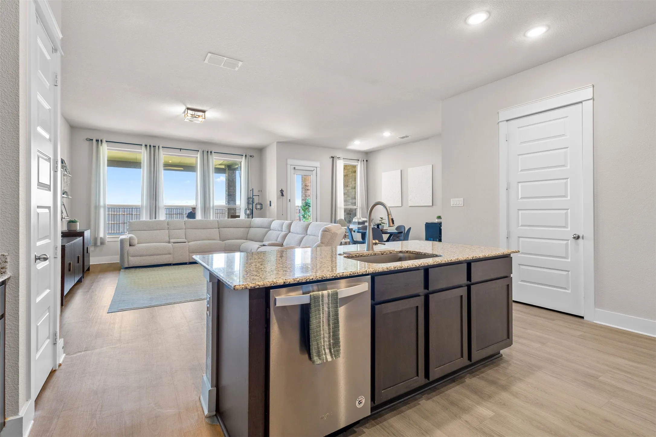 Open-concept living area featuring wood-finish flooring, recessed lighting, and a kitchen island with a built-in stainless steel dishwasher