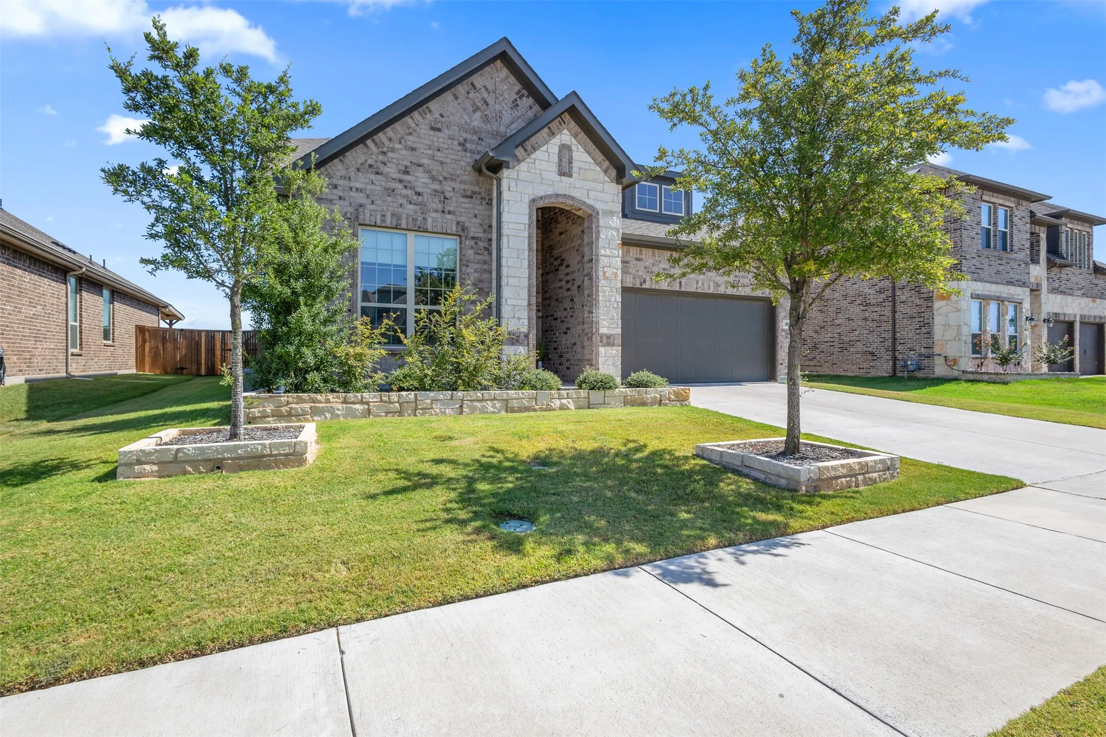 Brick facade with stone accents, arched entryway, attached garage, and mature landscaping