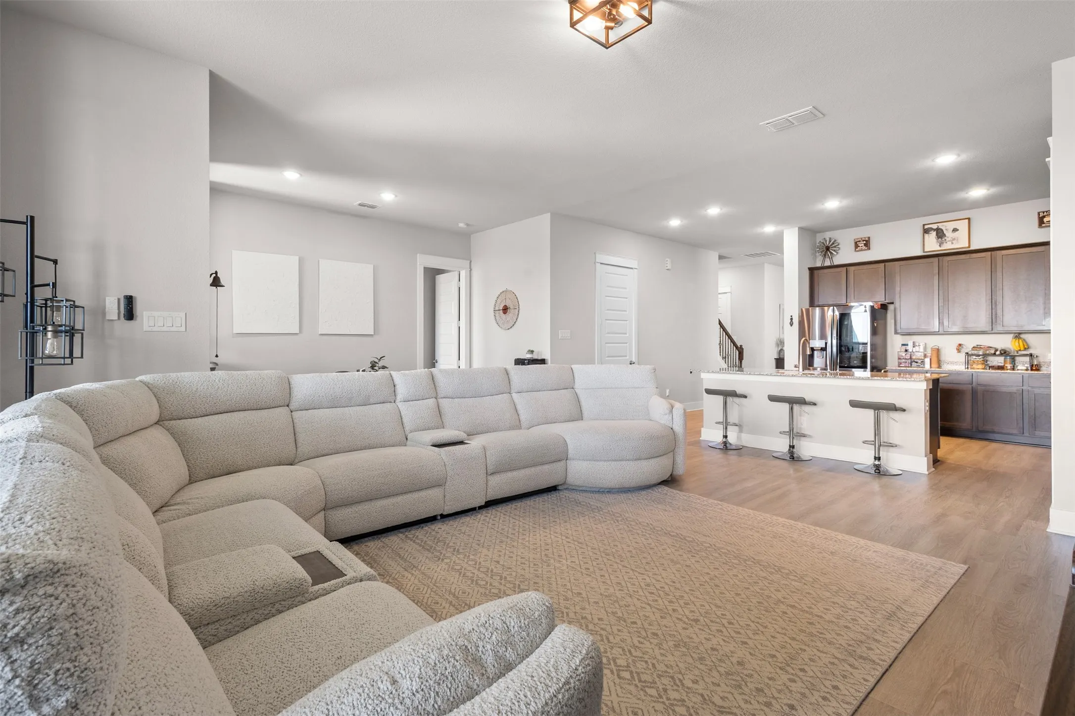 Open-concept living area featuring wood-finish flooring, recessed lighting, a kitchen island with seating, dark wood cabinetry, and stainless steel appliances
