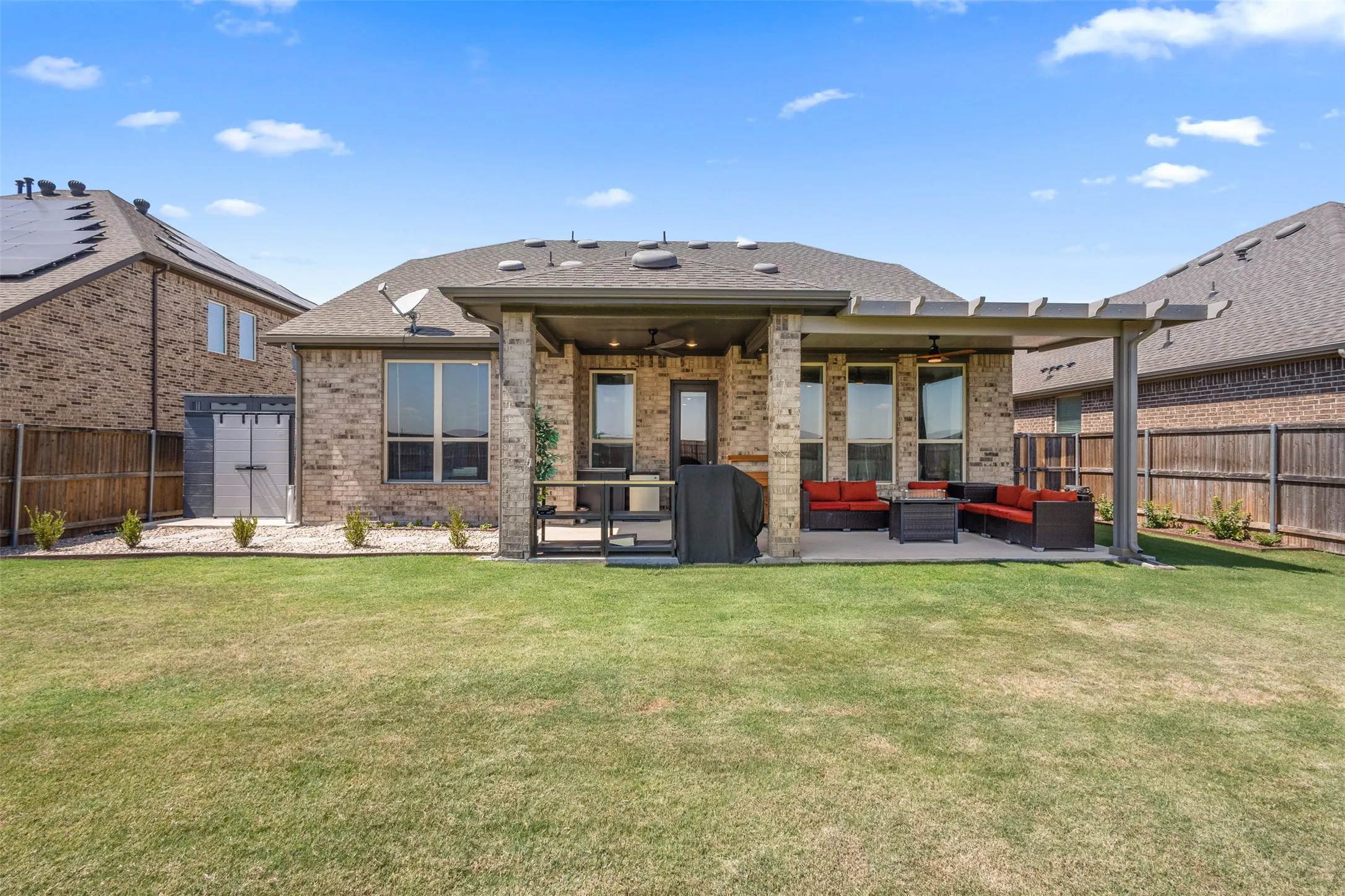 Expansive backyard featuring a covered patio, additional pergola, brick exterior, and a storage shed