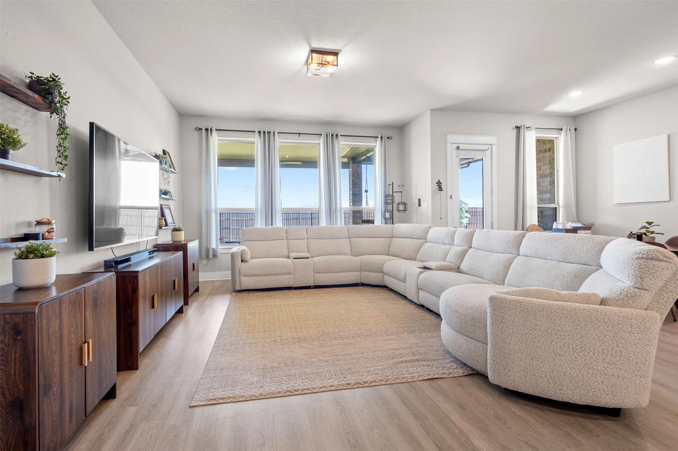 Expansive living area featuring light wood-finish flooring, recessed lighting, and large windows with privacy drapes