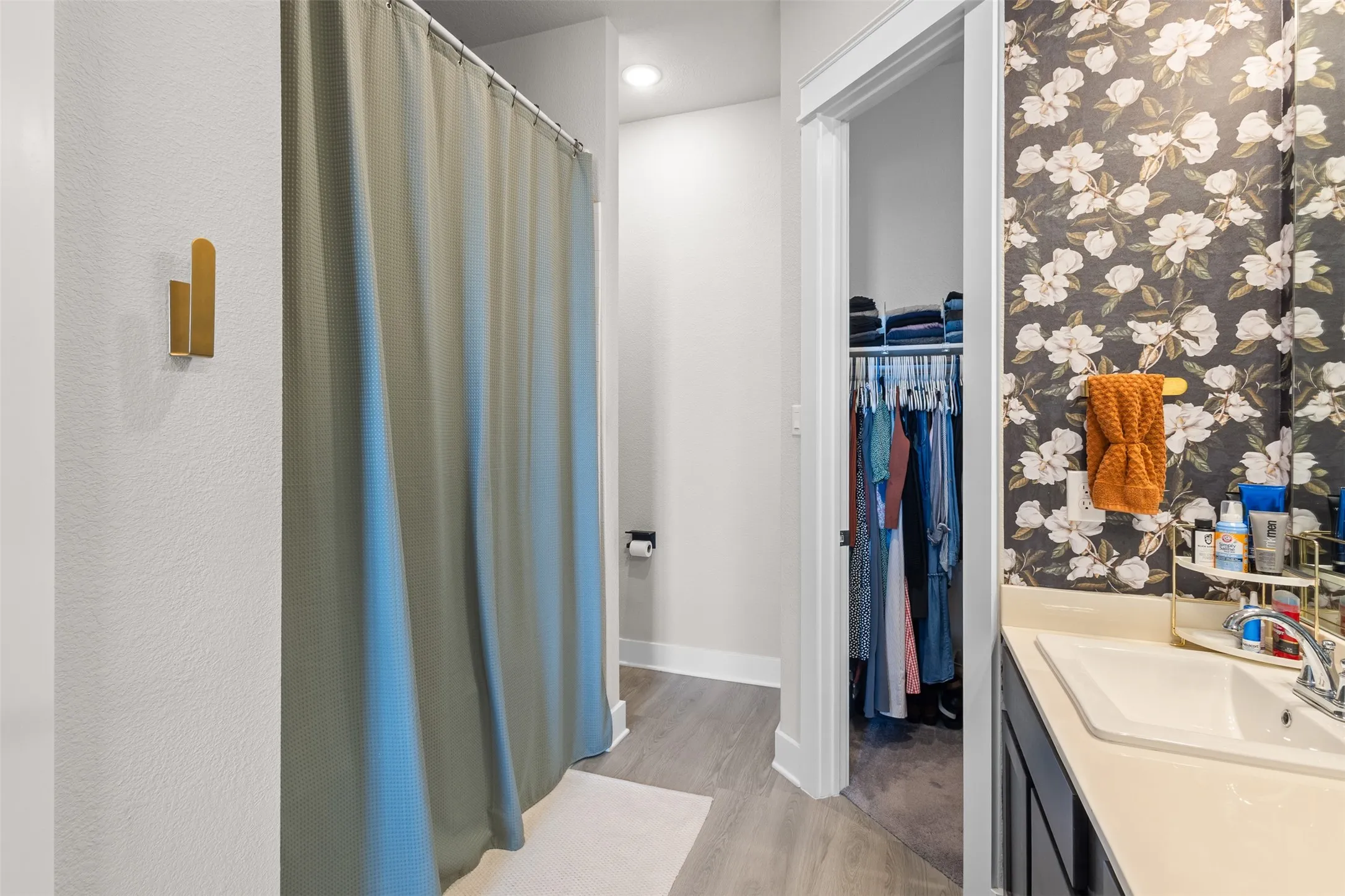 White vanity with integrated sink, patterned accent wall, recessed lighting, and wood-finish flooring