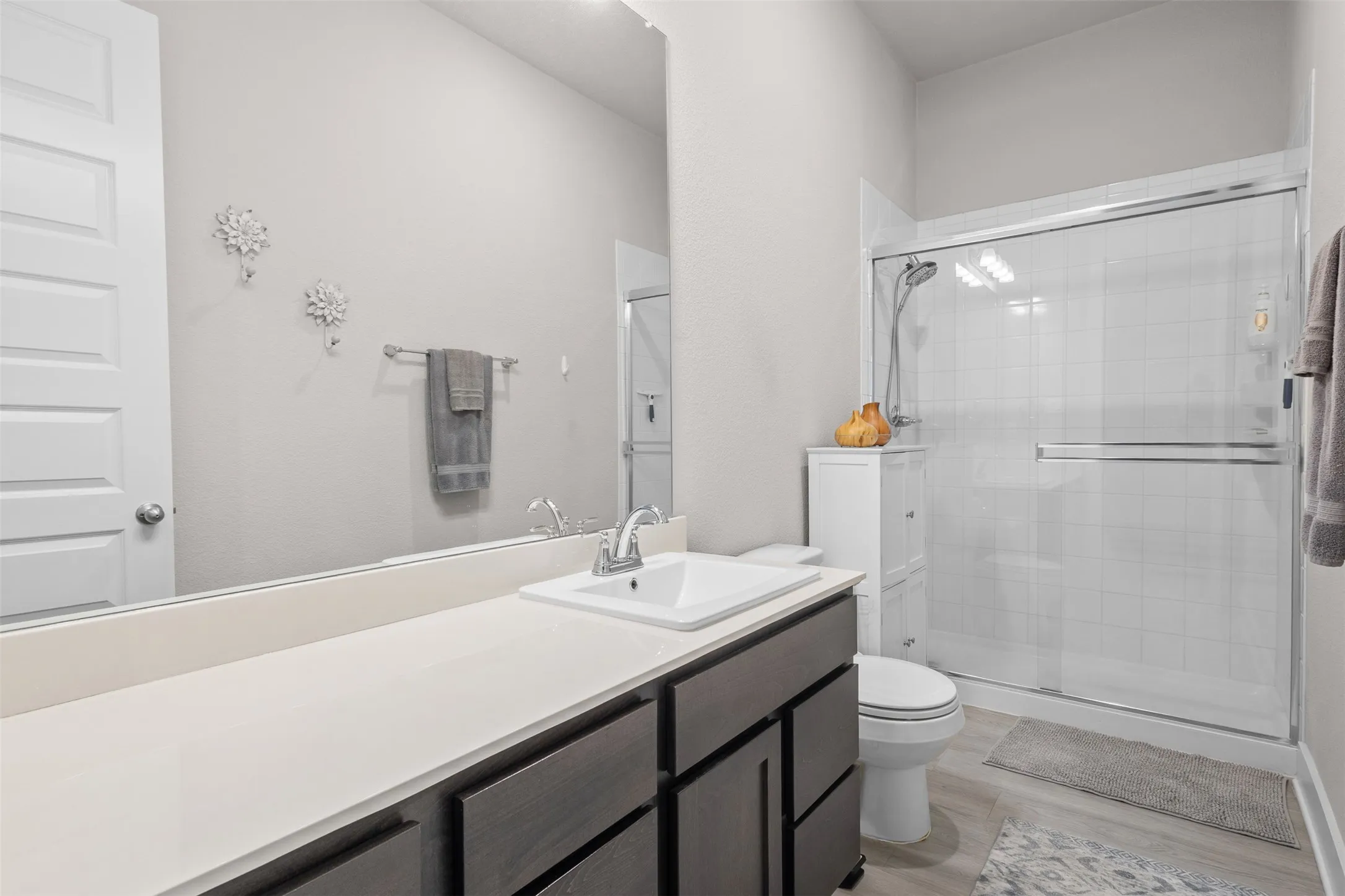 Vanity with an integrated sink and light-colored countertop, dark wood-finish cabinetry, a large wall-mounted mirror, and a shower with a sliding glass door