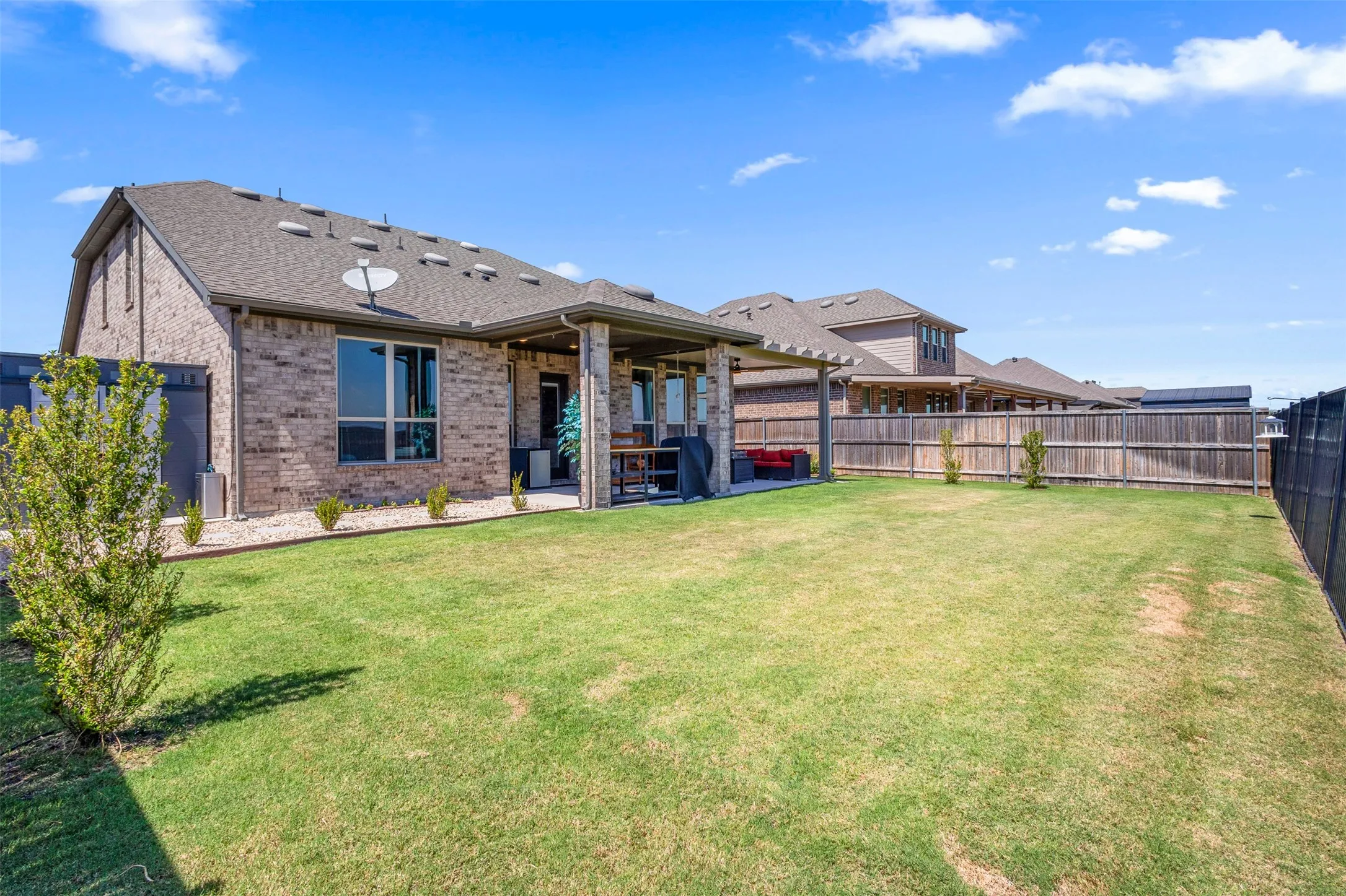 Expansive backyard with a manicured lawn, brick exterior, and covered patio featuring a wood pergola