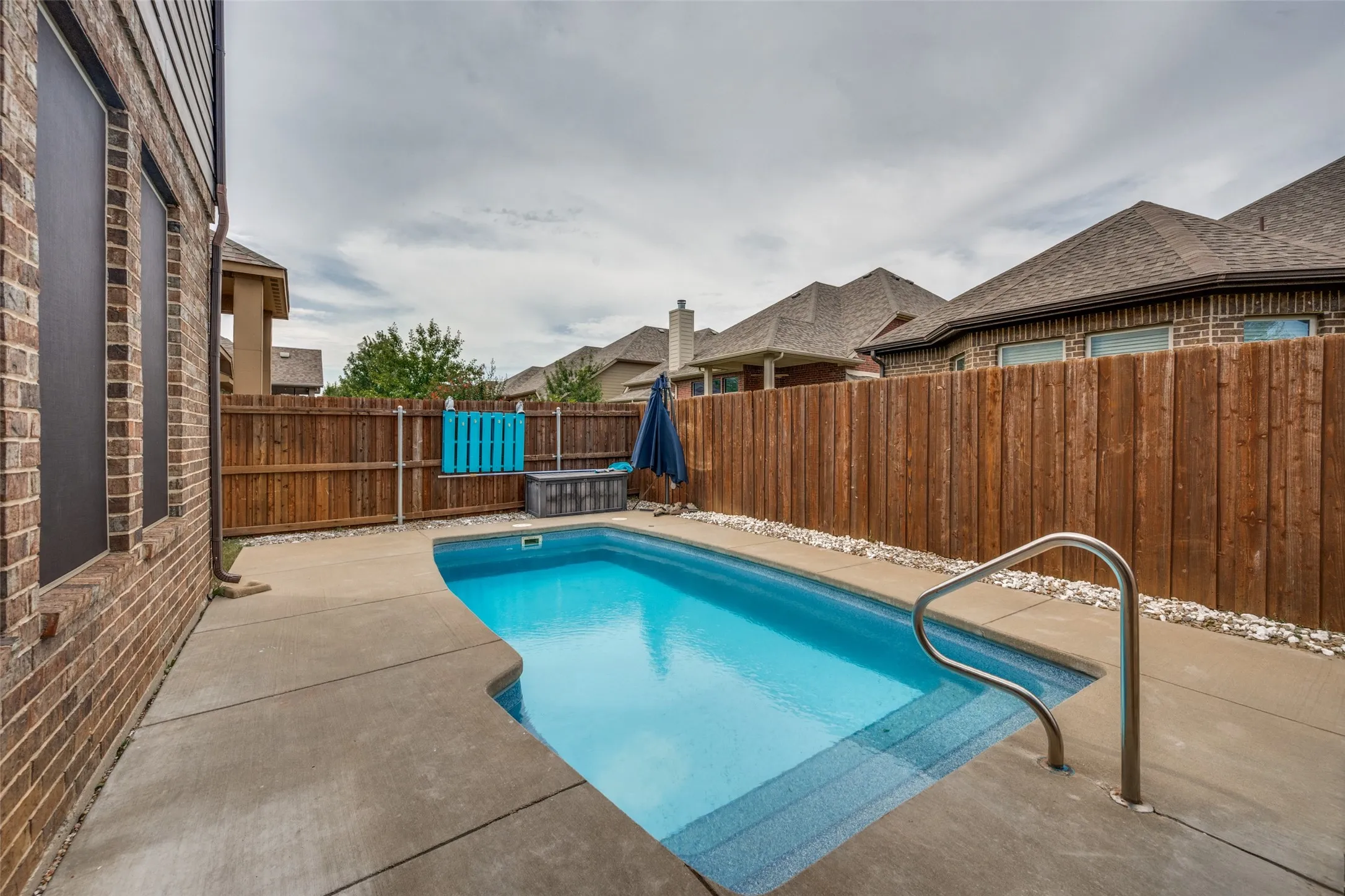 Private backyard featuring a swimming pool with integrated steps, concrete surround, and a privacy fence