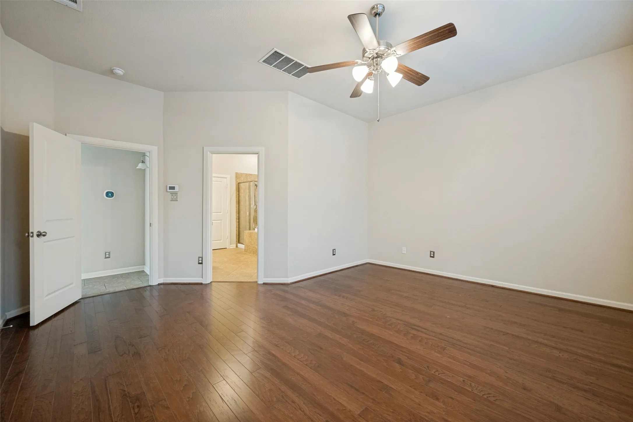 Spacious Master bedroom featuring wood-finish flooring, light neutral wall tones, and a ceiling fan with integrated lighting
