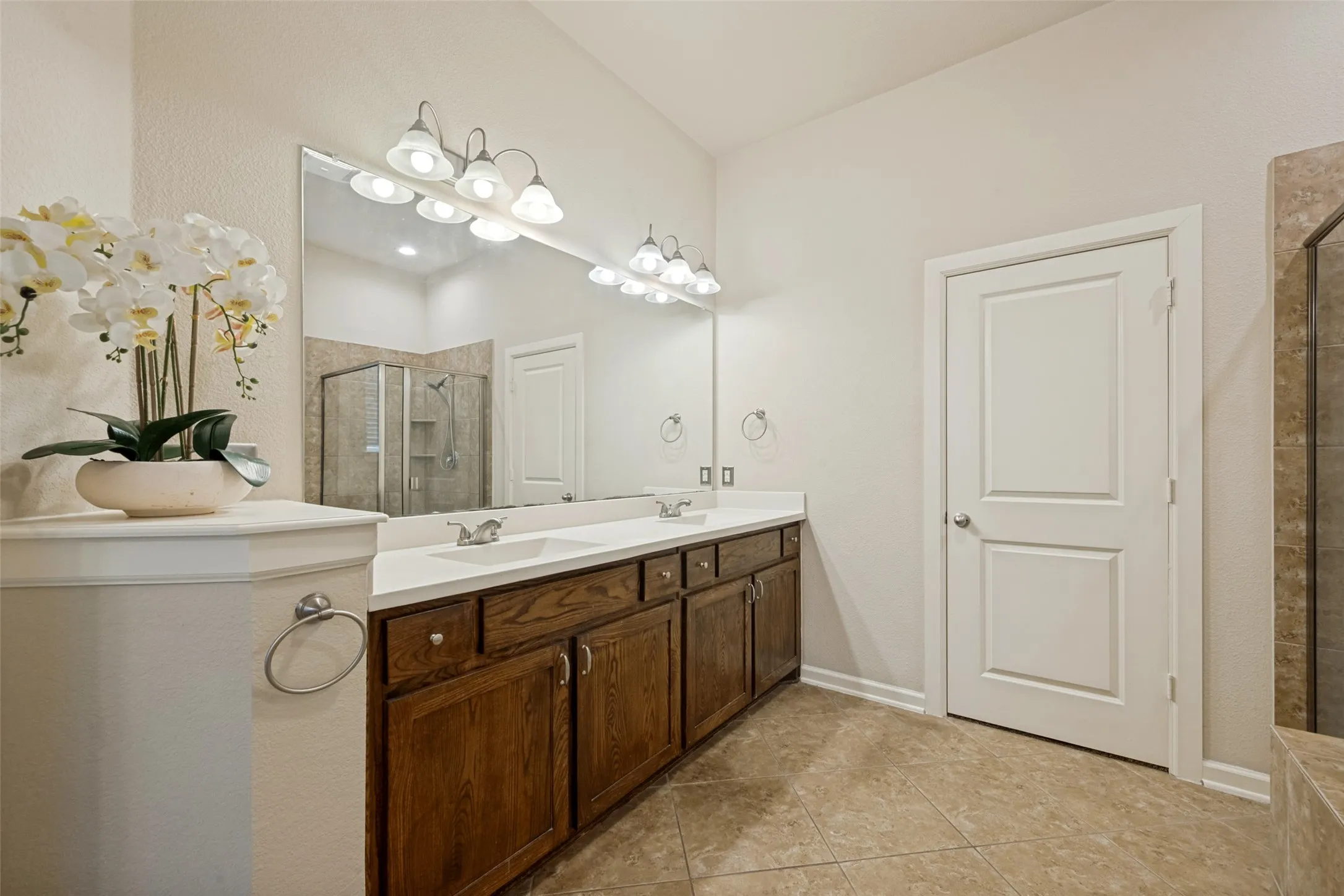 Master bathroom with double vanity with integrated sinks, wood-finish cabinetry, a large wall-mounted mirror, and tile flooring