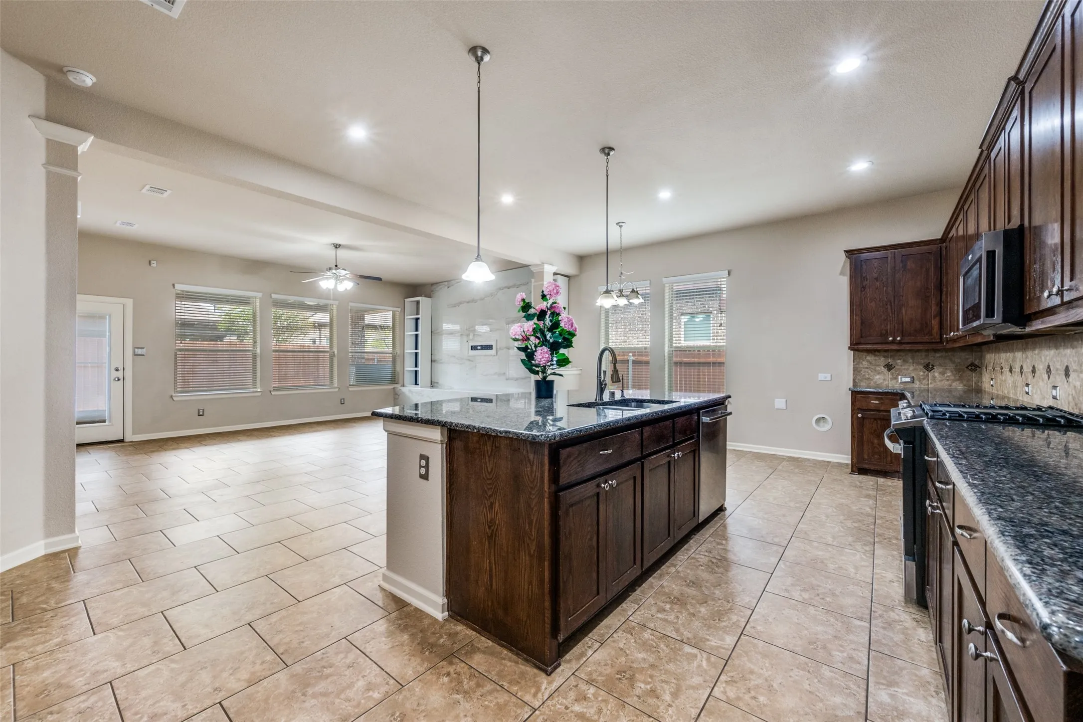 Spacious open-concept living area featuring tile flooring, a kitchen island with a built-in sink, dark wood cabinetry, and recessed lighting