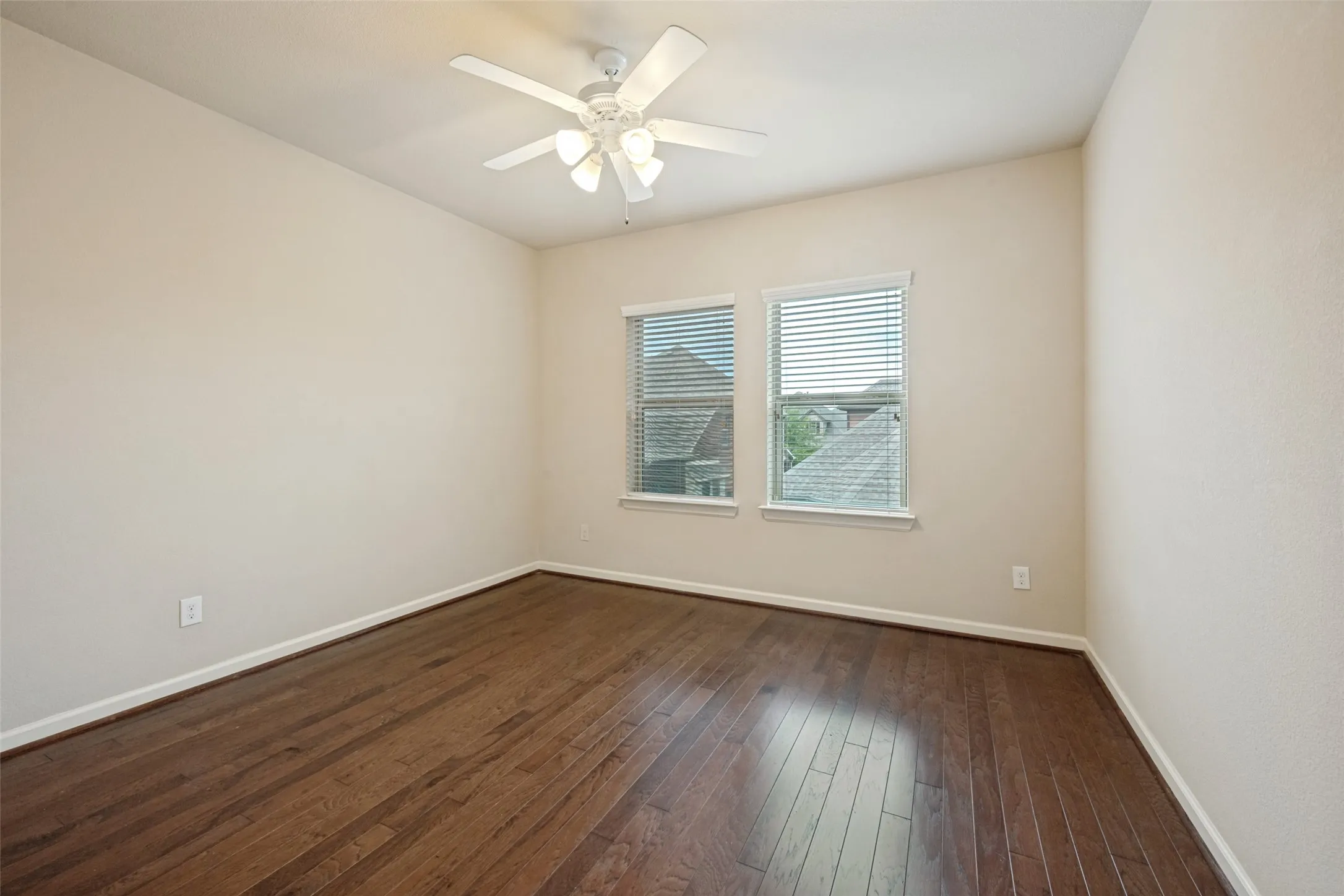 Wood-finish flooring, two windows with blinds, and a ceiling fan with integrated lighting