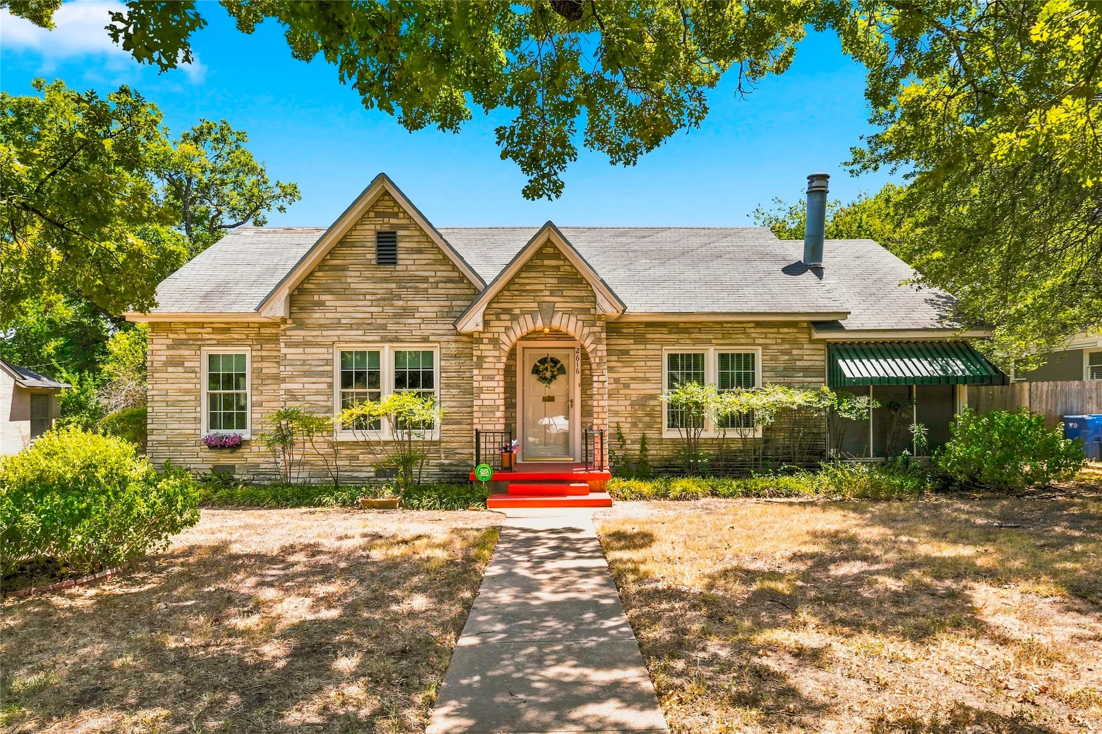 Stone exterior with gabled rooflines, arched entry, multiple windows, and a covered porch with an awning