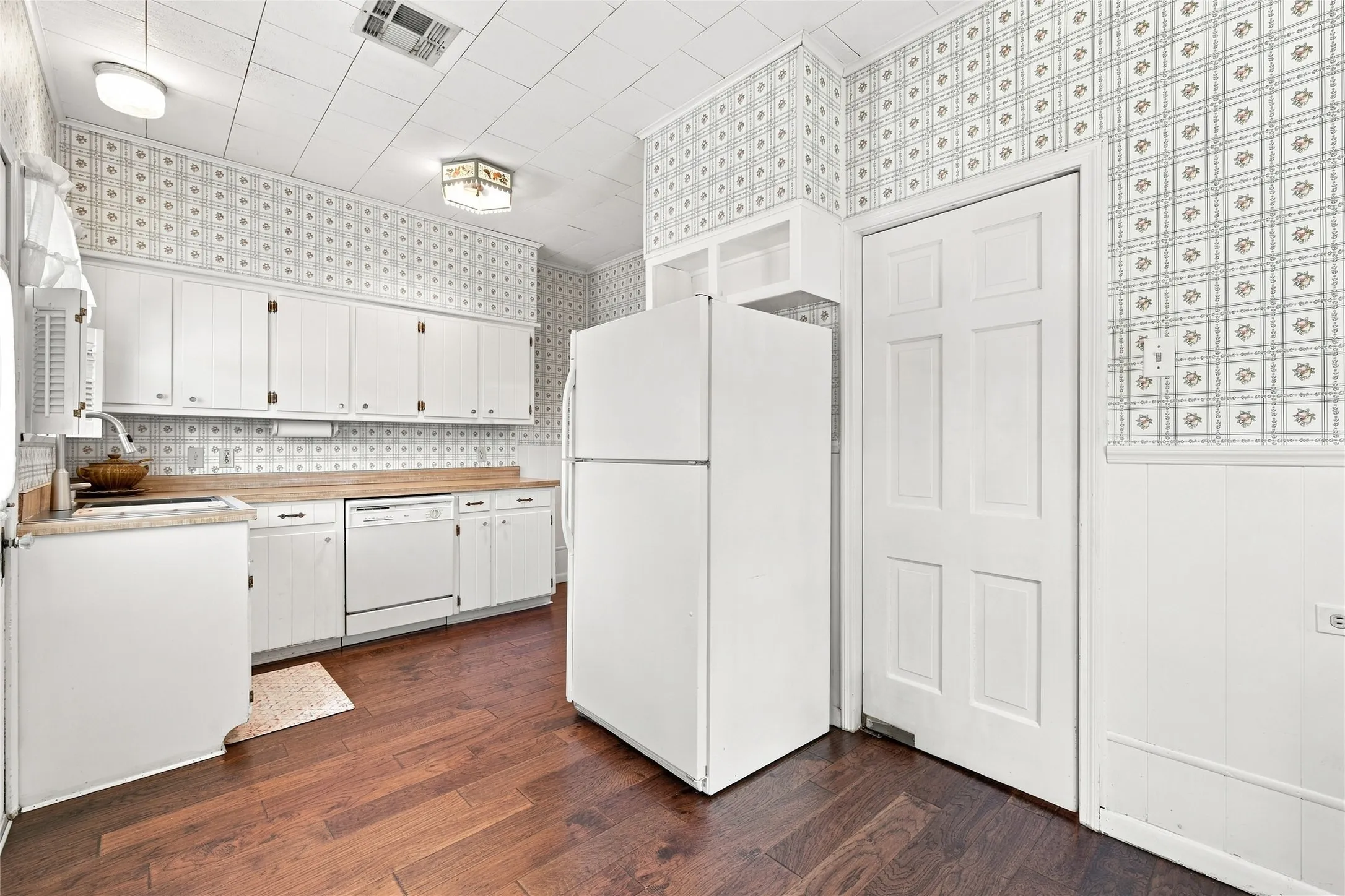 White cabinetry, wood-finish flooring, patterned wallpaper, ceiling paneling, and a flush-mount ceiling light fixture