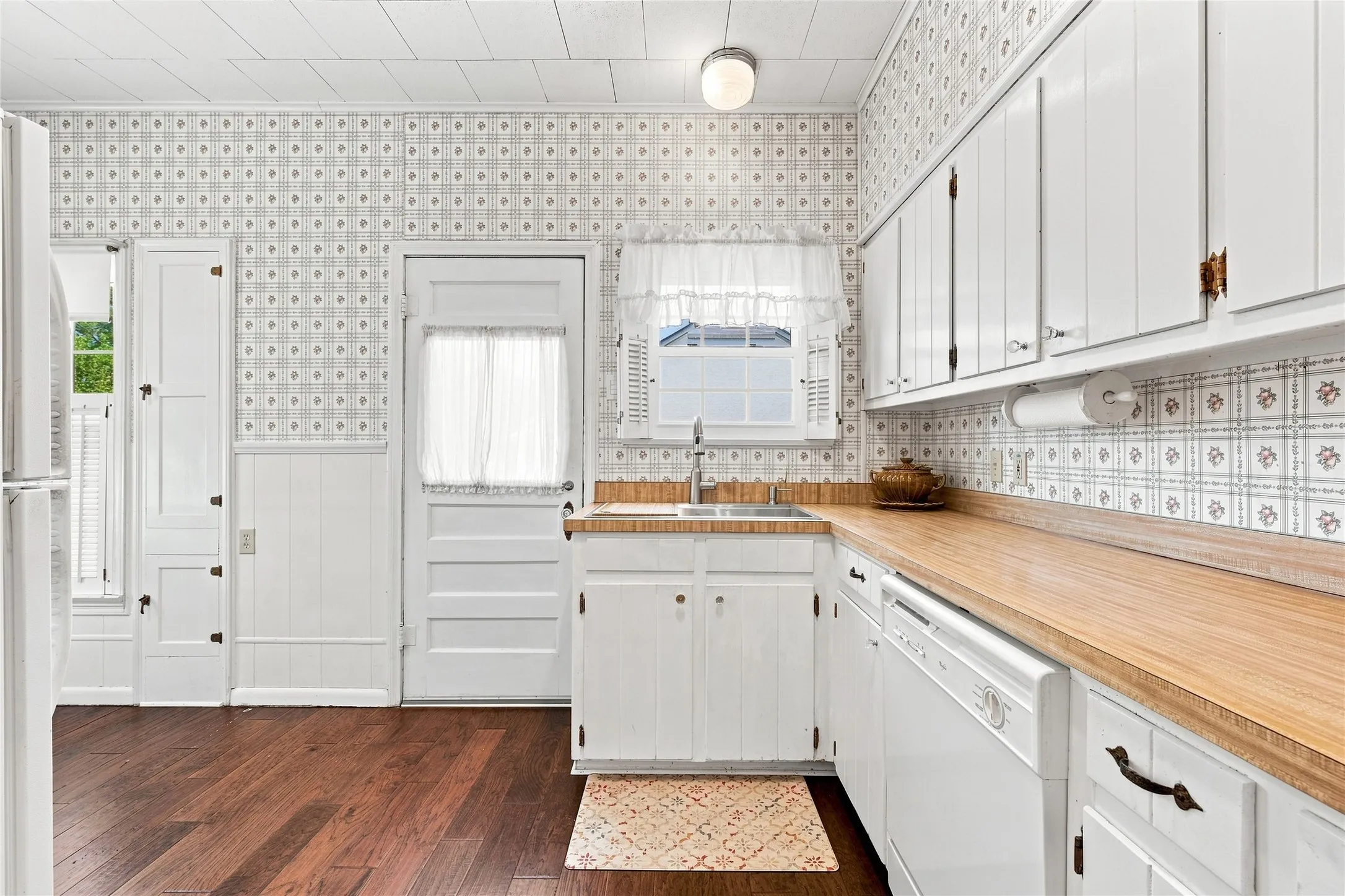 Kitchen featuring wood-finish flooring, white cabinetry, a double basin sink, and a dishwasher