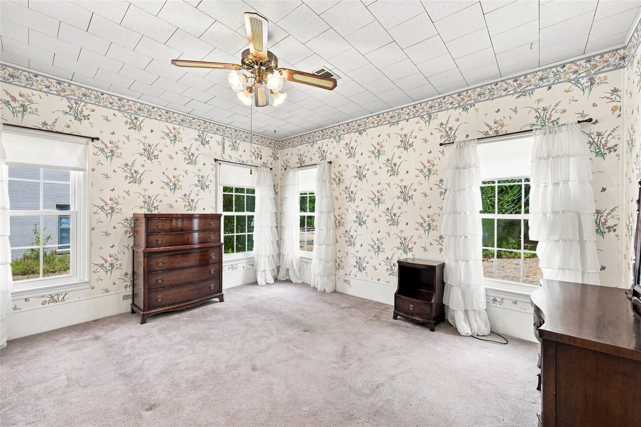 Wallpapered walls, multiple windows, ceiling fan with light fixture, light-toned carpeting, and white window trim