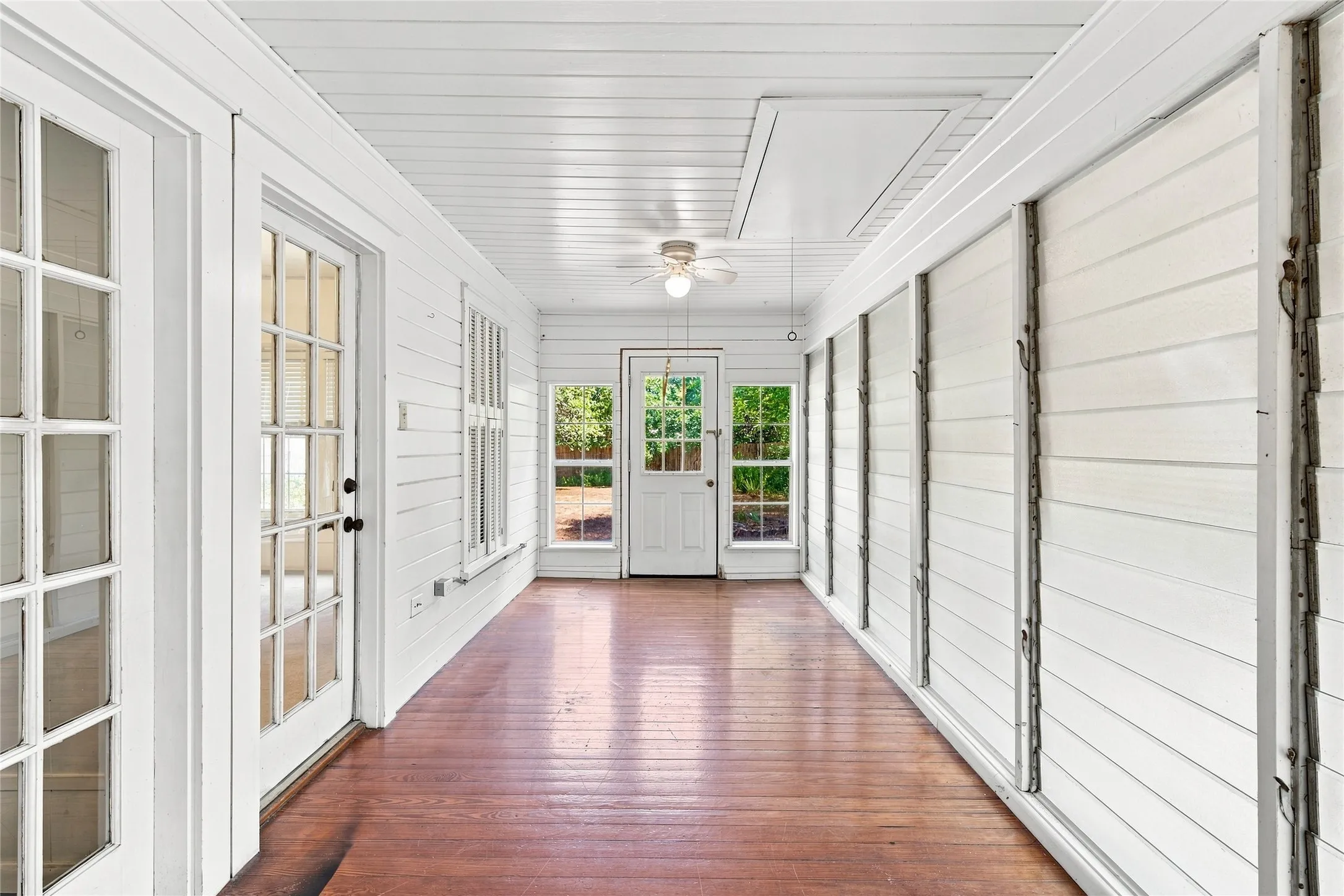 Hardwood flooring throughout, multiple paneled glass doors, white shiplap walls, recessed ceiling fan, and large windows