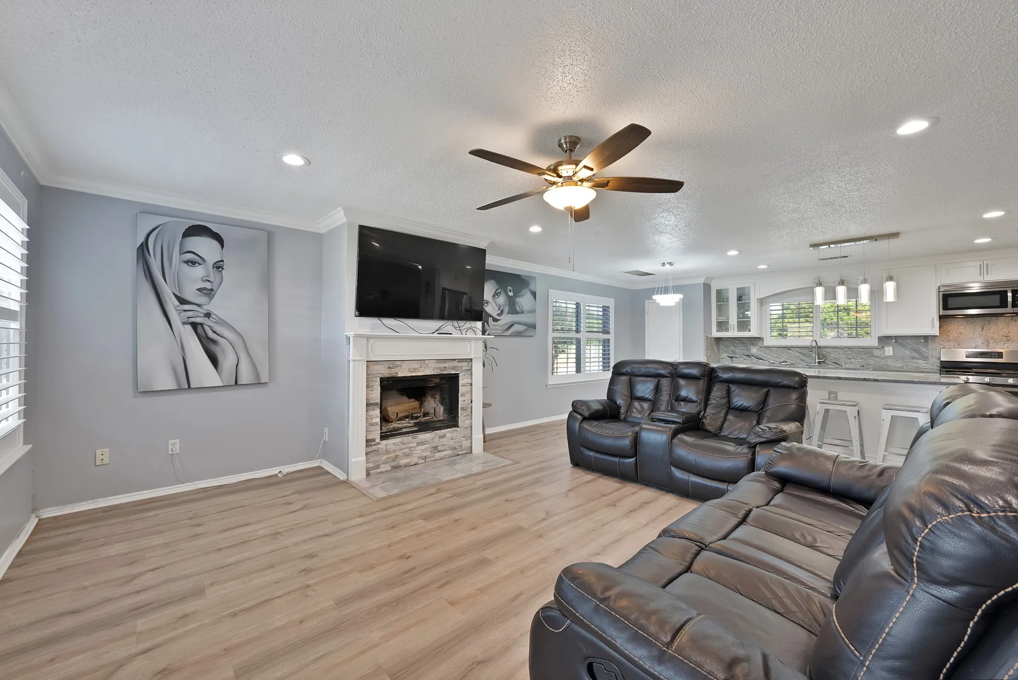 Open-concept living area featuring wood-finish flooring, a stone-clad fireplace, and recessed lighting