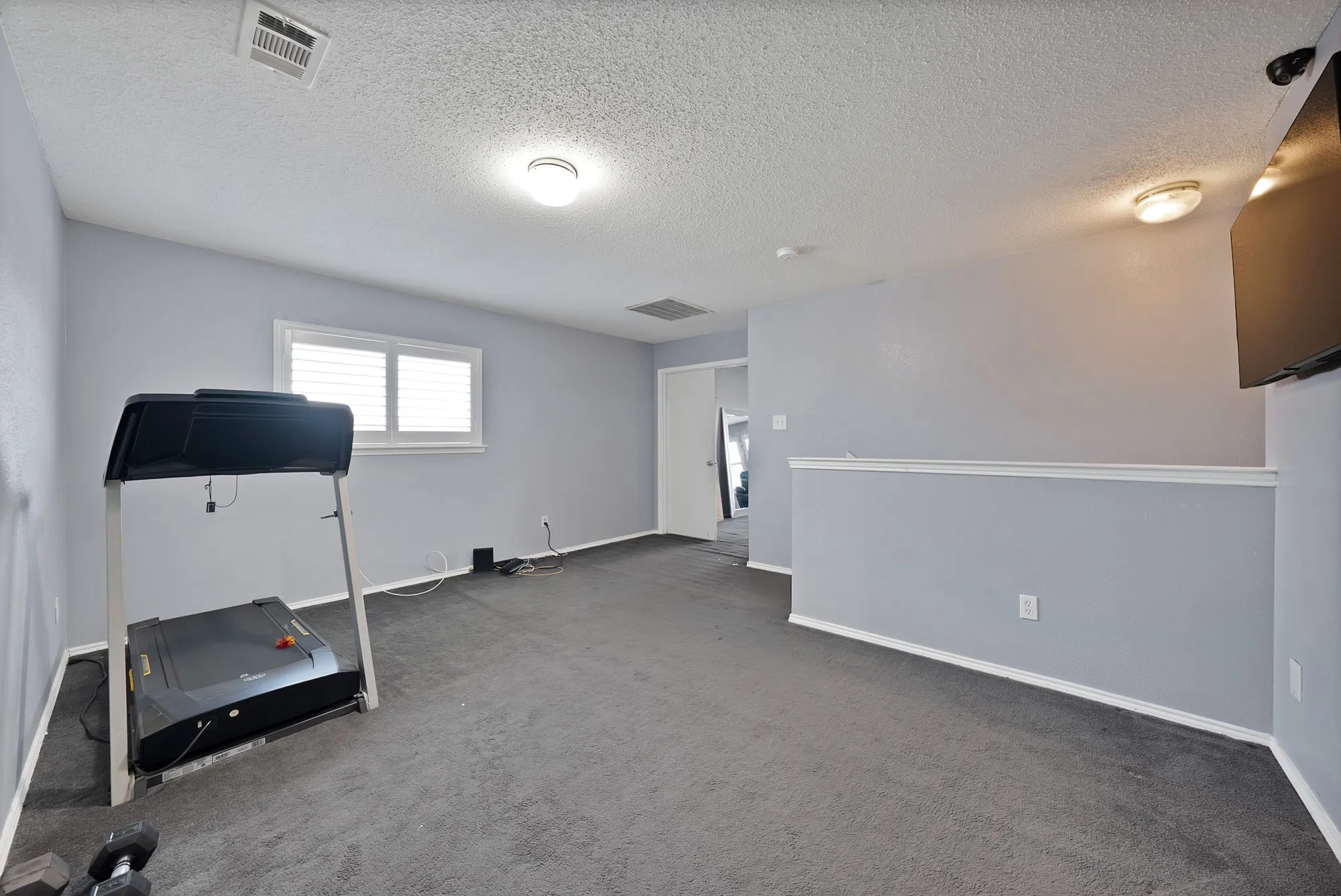 Carpeted space featuring a window with white shutters, a partial wall, and overhead lighting