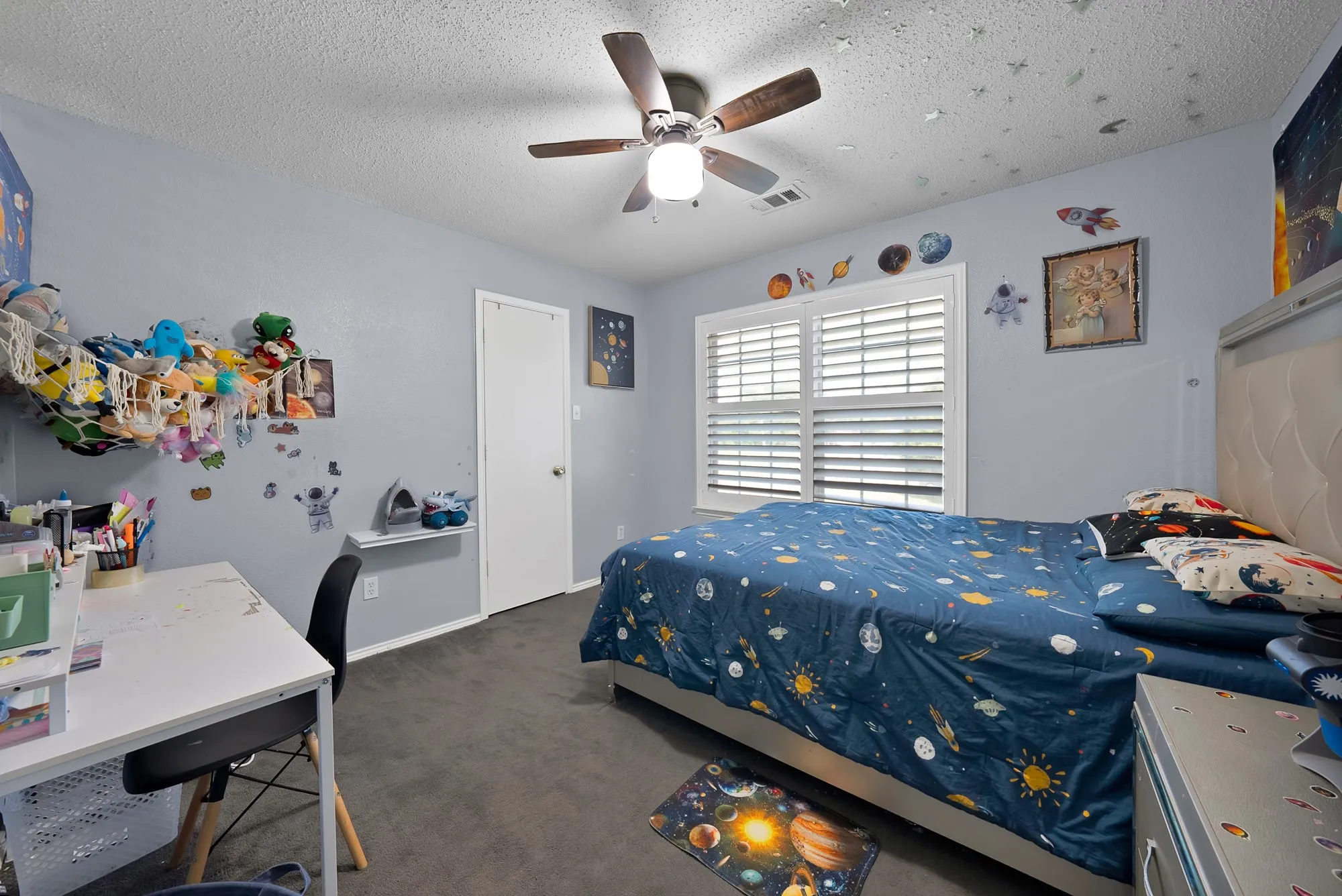 Textured ceiling with a ceiling fan, window with white louvered shutters, light gray wall paint, and gray carpet flooring