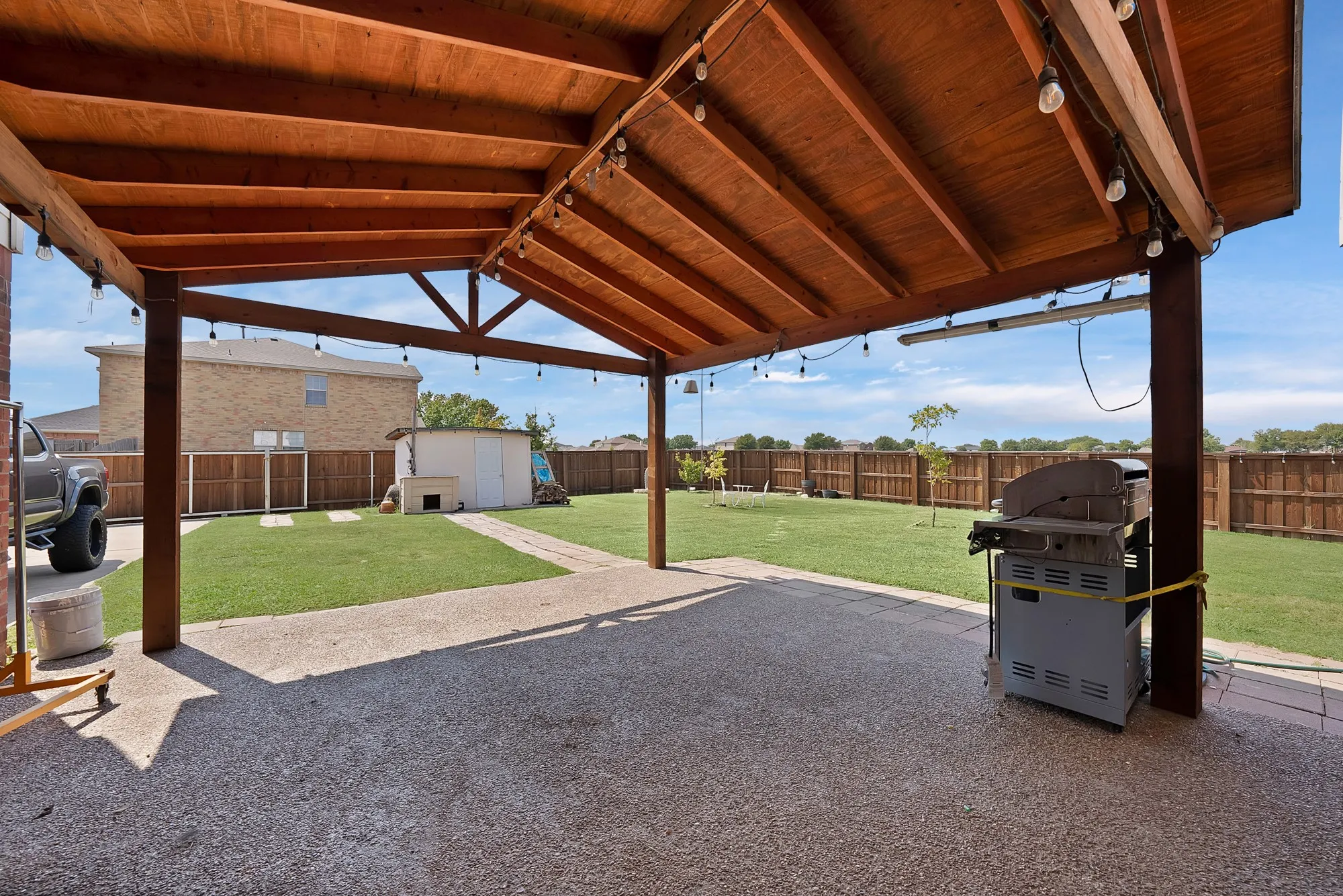 Expansive backyard featuring a covered patio with wood beam construction, concrete flooring, and a manicured lawn
