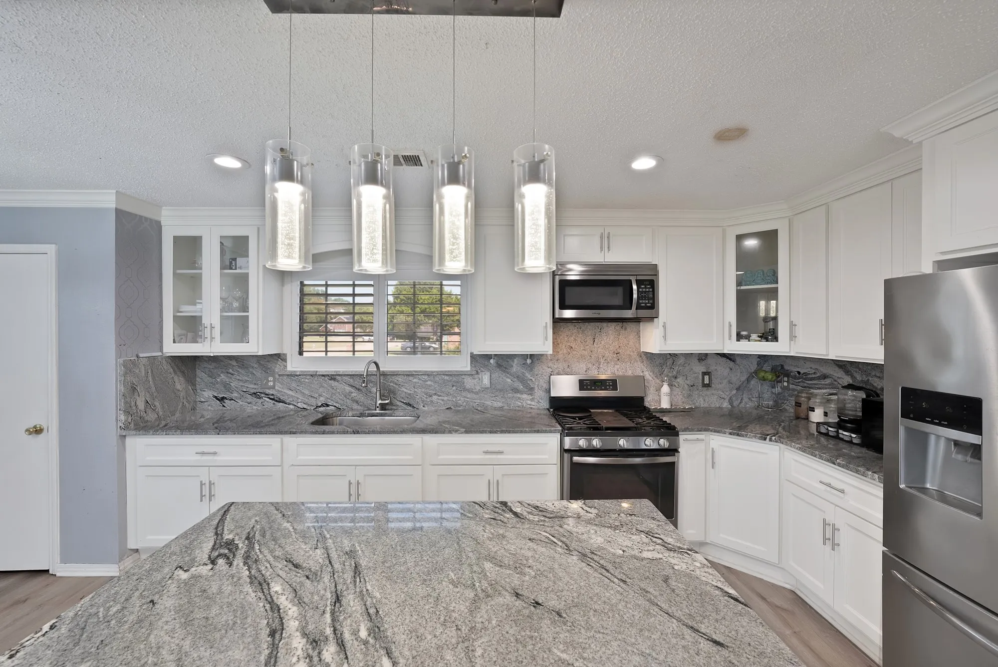 White cabinetry with glass-front accents, stainless steel appliances, a kitchen island with stone countertops, and pendant lighting