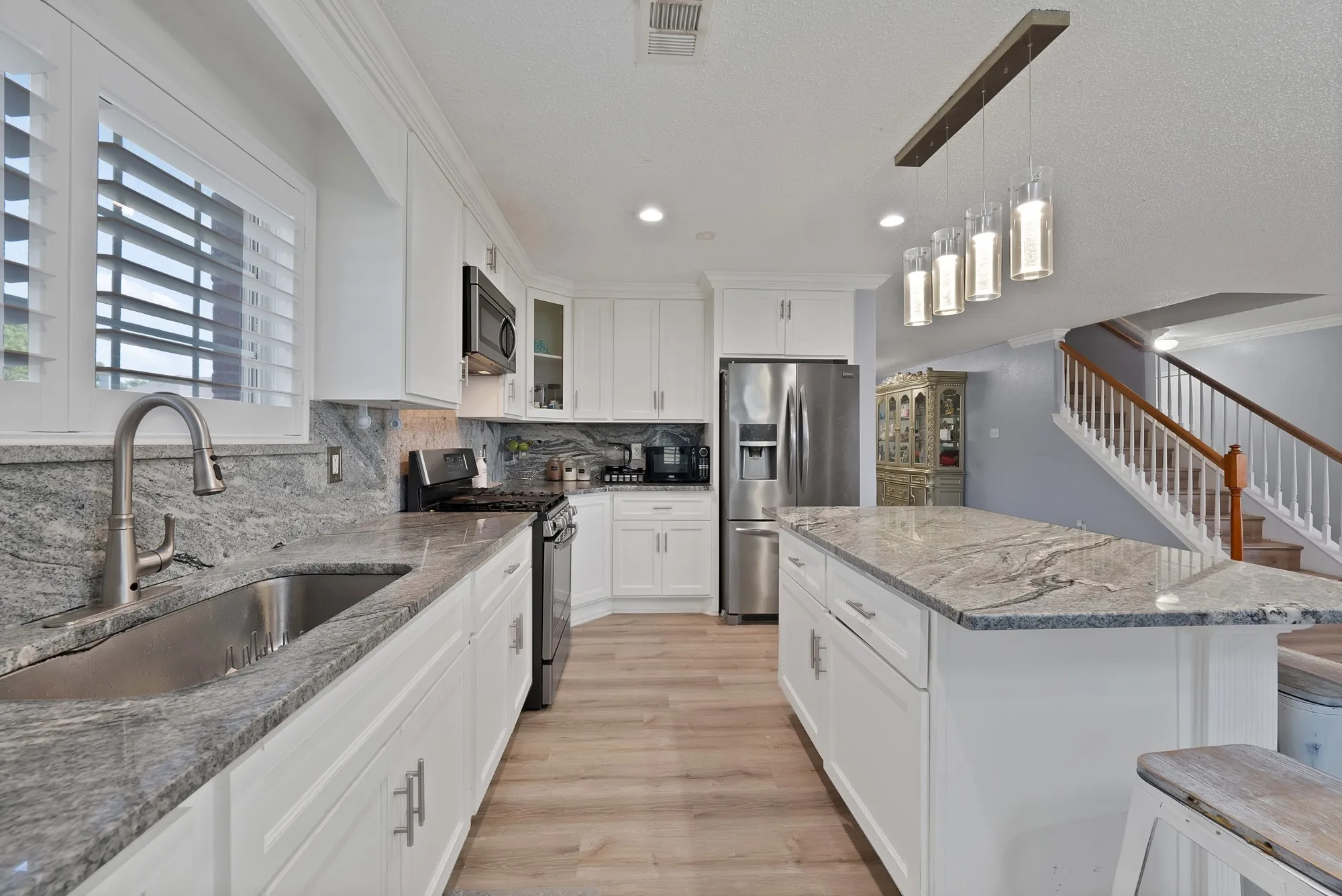 White cabinetry with brushed nickel hardware, stainless steel appliances, granite countertops, wood-finish flooring, and a kitchen island with pendant lighting