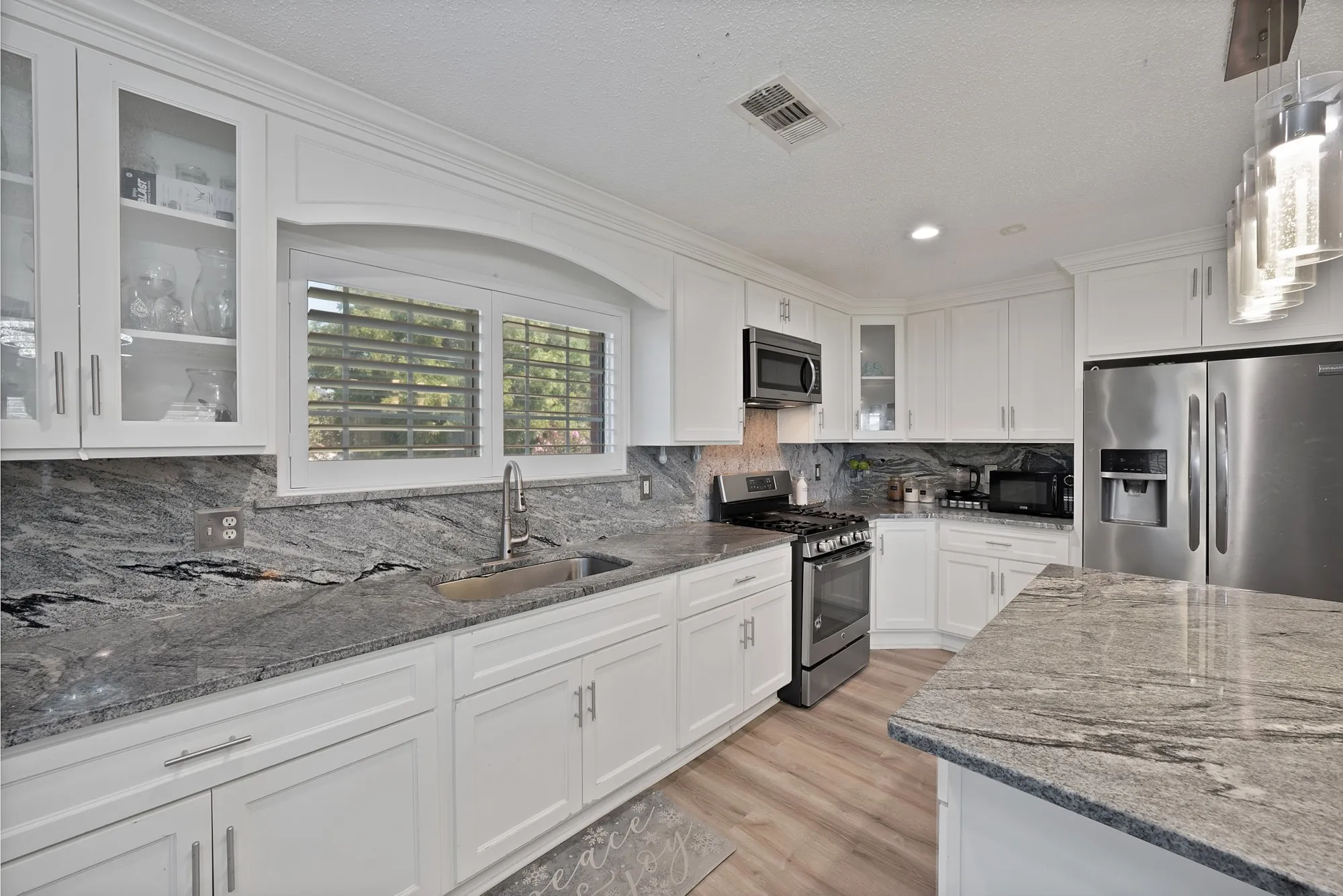 White shaker-style cabinetry, stainless steel appliances, grey stone countertops, wood-finish flooring, and an island with stone countertop