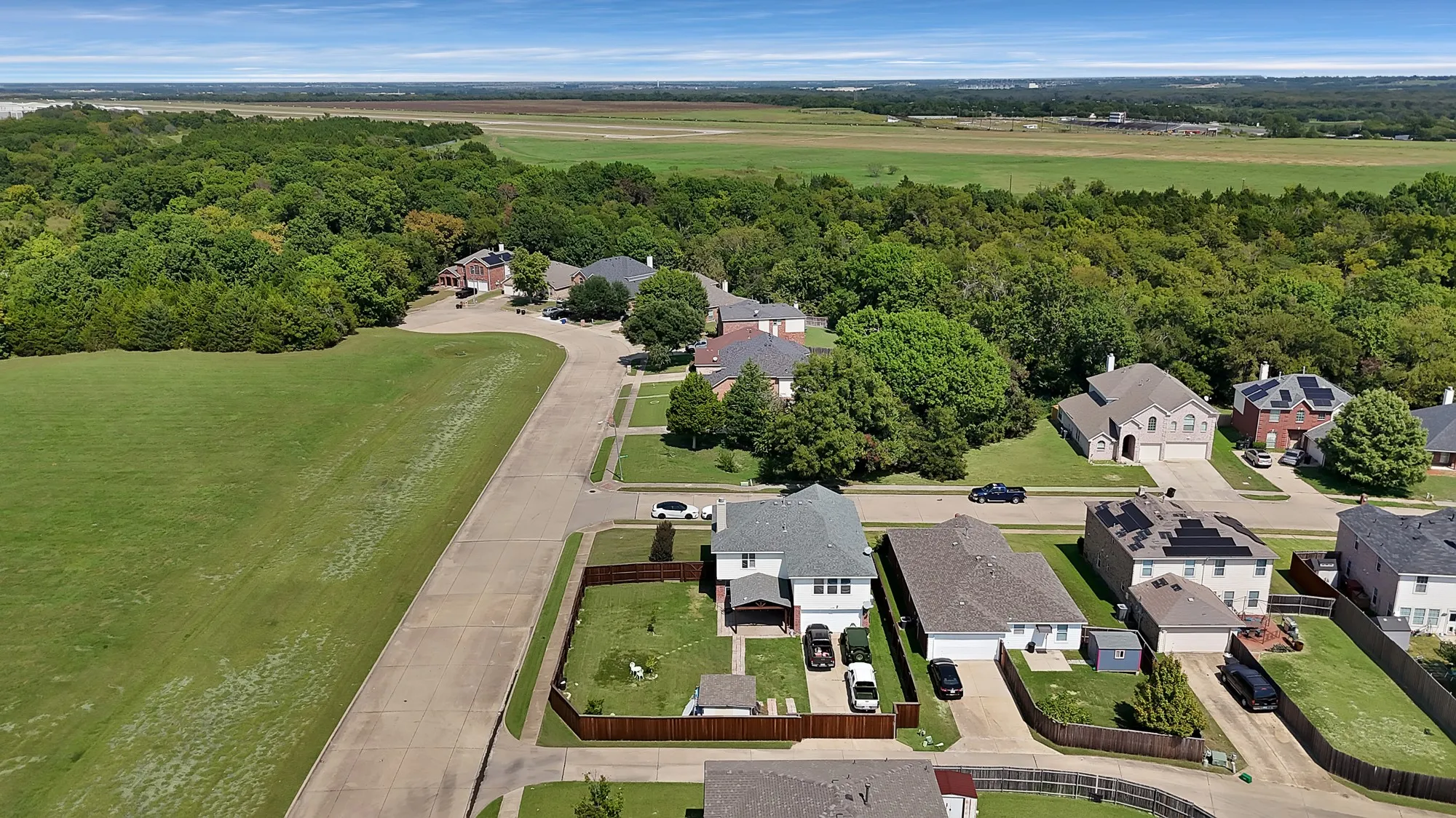 Aerial perspective showcasing a residential street bordered by expansive green spaces and mature trees