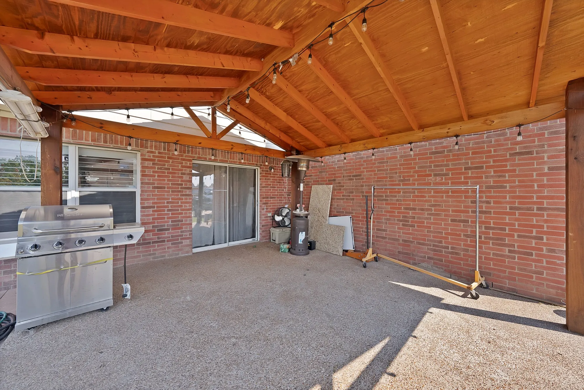 Covered patio featuring a wood-beam ceiling, brick wall, and concrete flooring