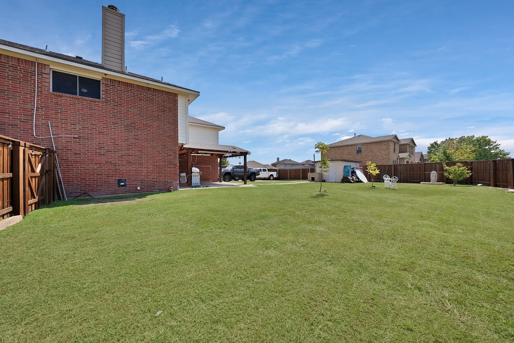 Expansive grassy yard with wood fencing and a covered patio structure