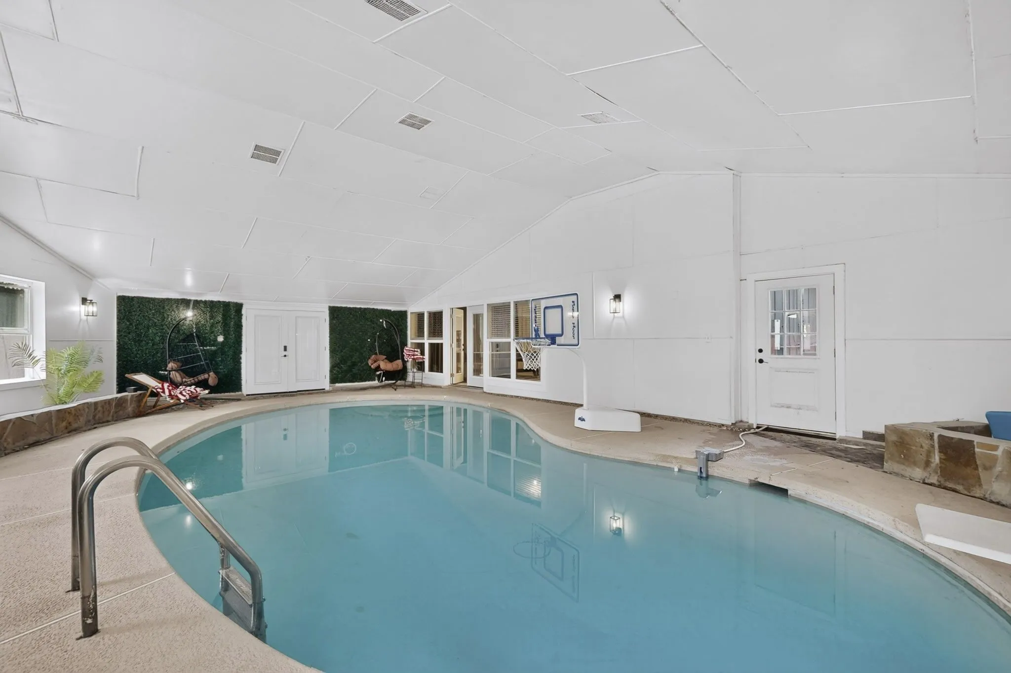 Indoor swimming pool with integrated steps, textured pool deck, stone-finish retaining wall, and multiple exterior doors