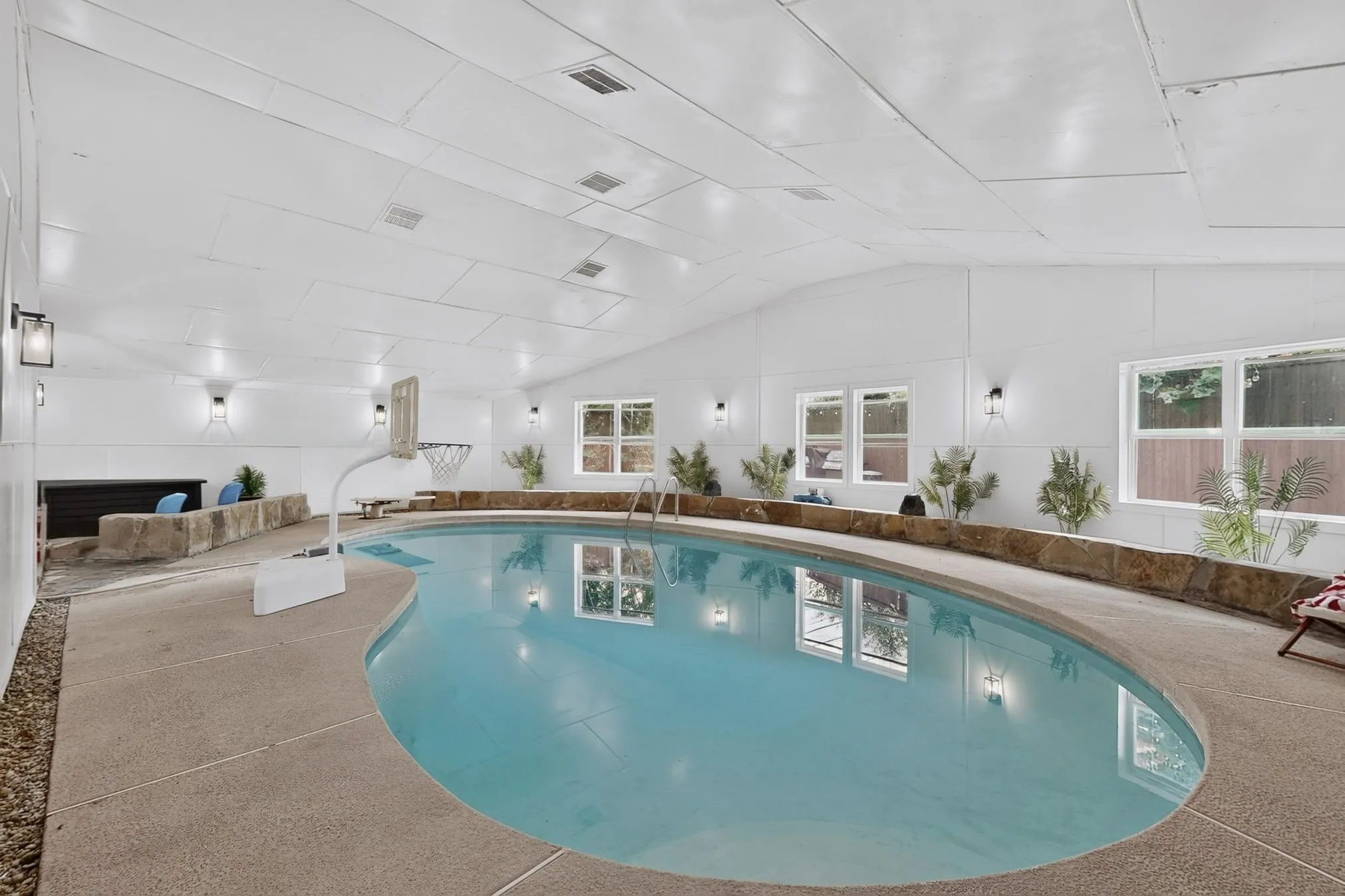 Indoor swimming pool with a curved edge, concrete decking, and stone wall accents