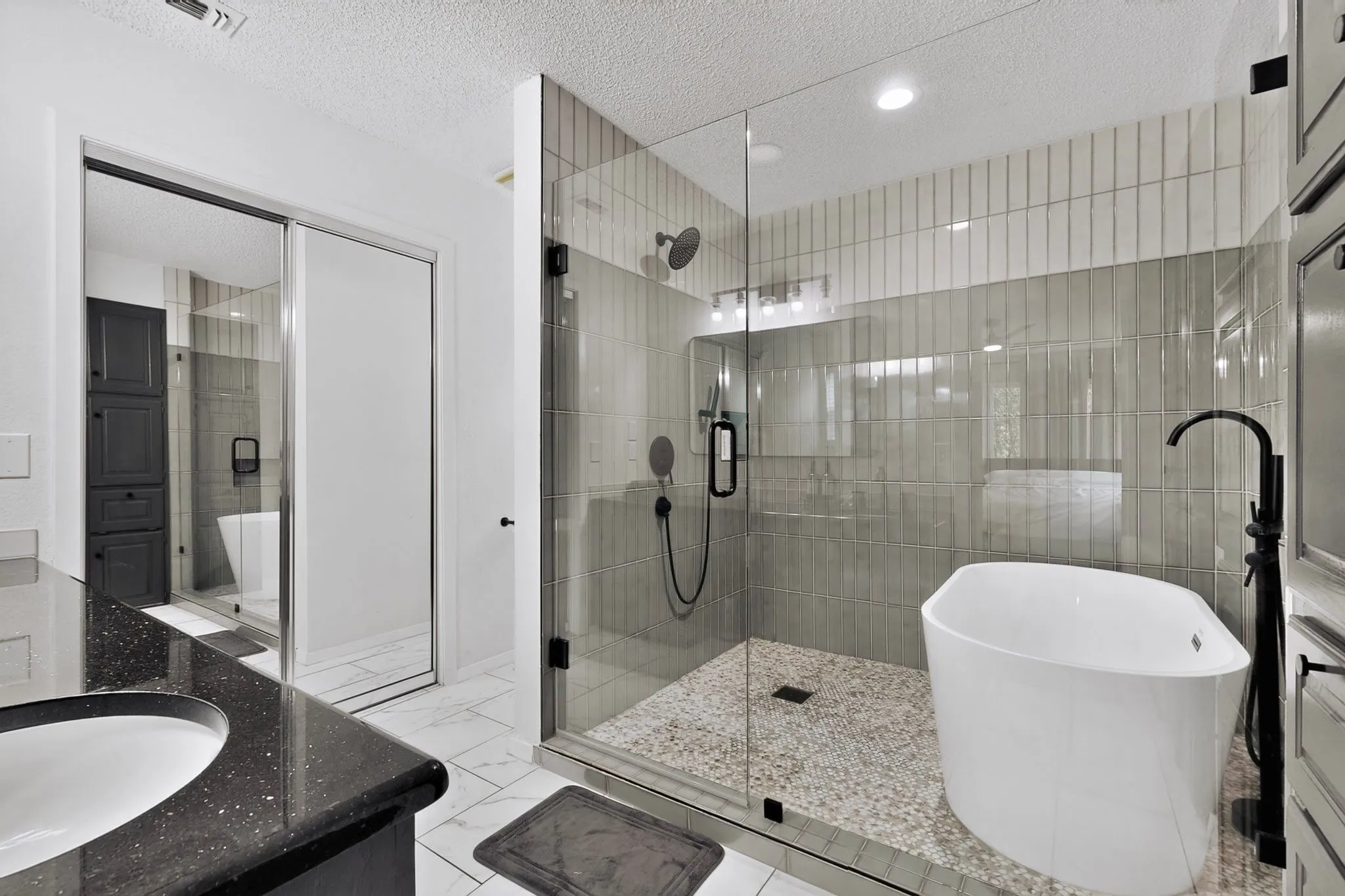 Glass-enclosed shower with a freestanding soaking tub, pebble tile shower floor, and textured vertical wall tile