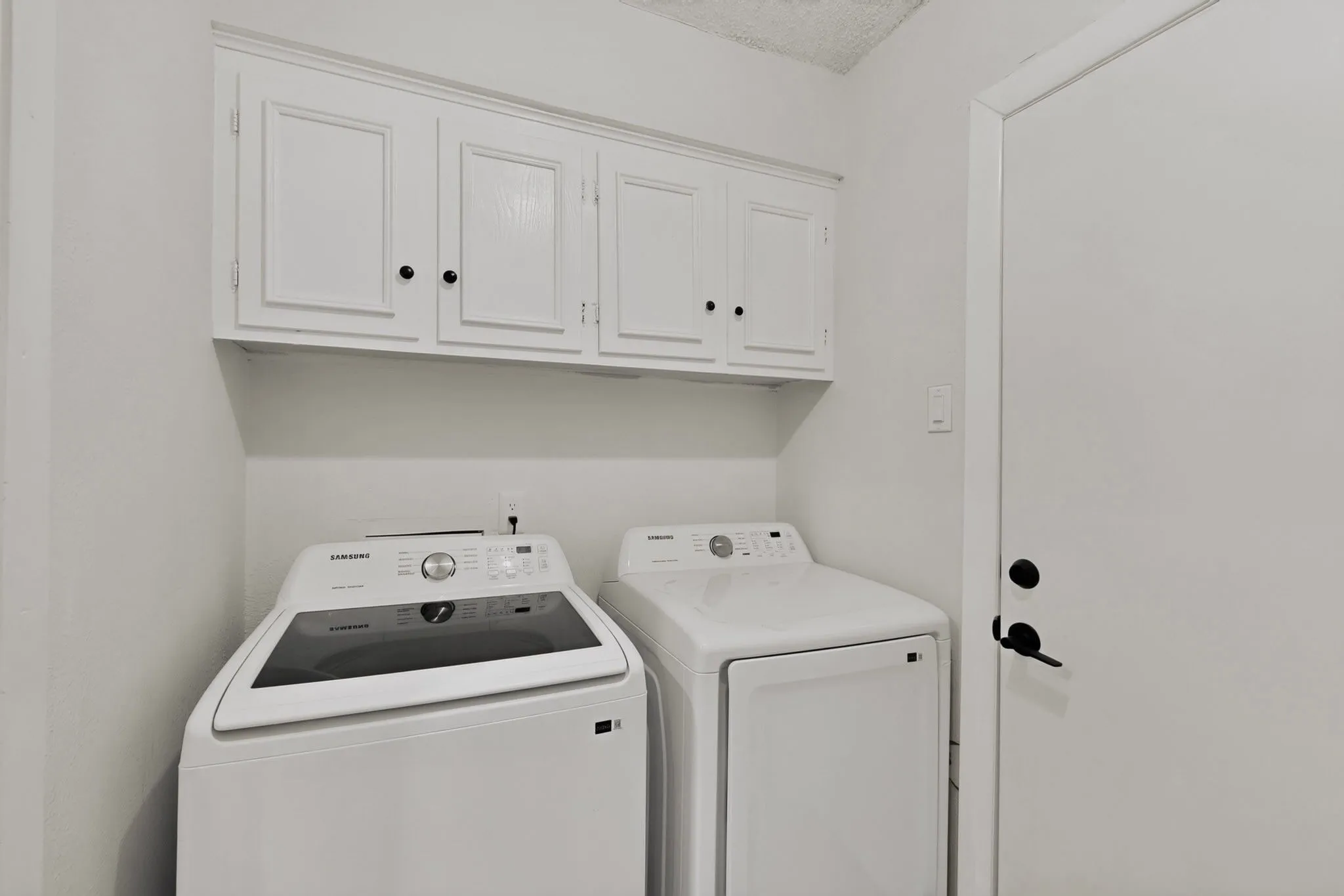 Dedicated laundry area featuring white cabinetry with black hardware