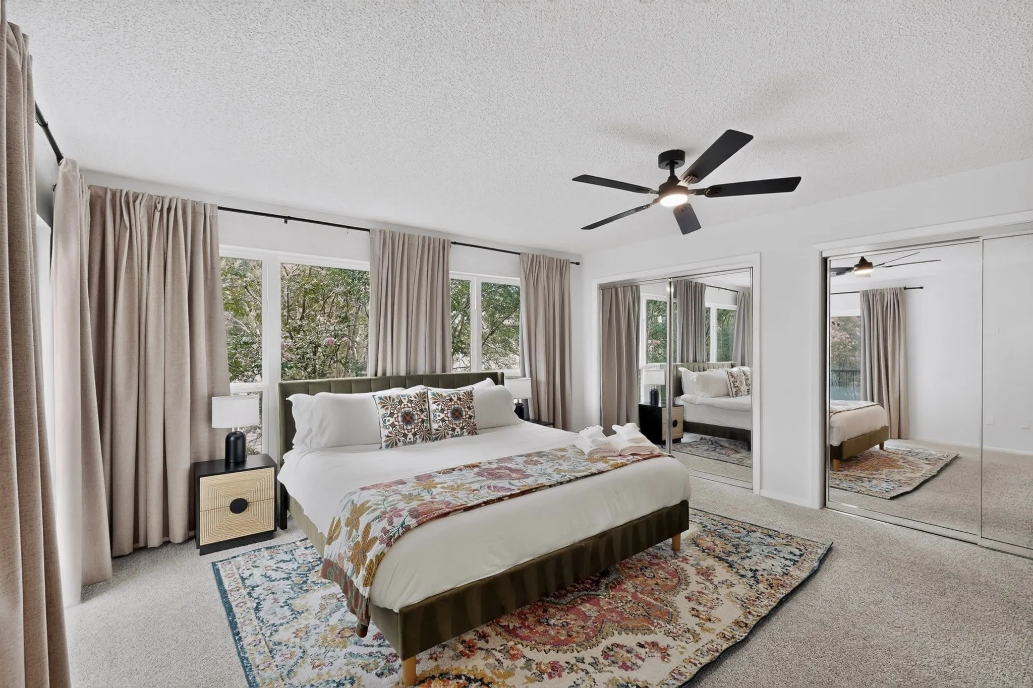 Full-height windows with light-filtering curtains, overhead ceiling fan with lighting, wall-to-wall carpeting, and mirrored sliding closet doors