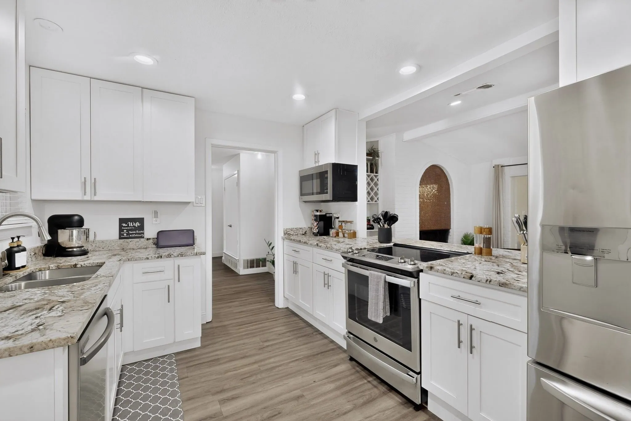 Kitchen featuring white shaker cabinetry, light-toned countertops, stainless steel appliances, wood-finish flooring, and recessed lighting