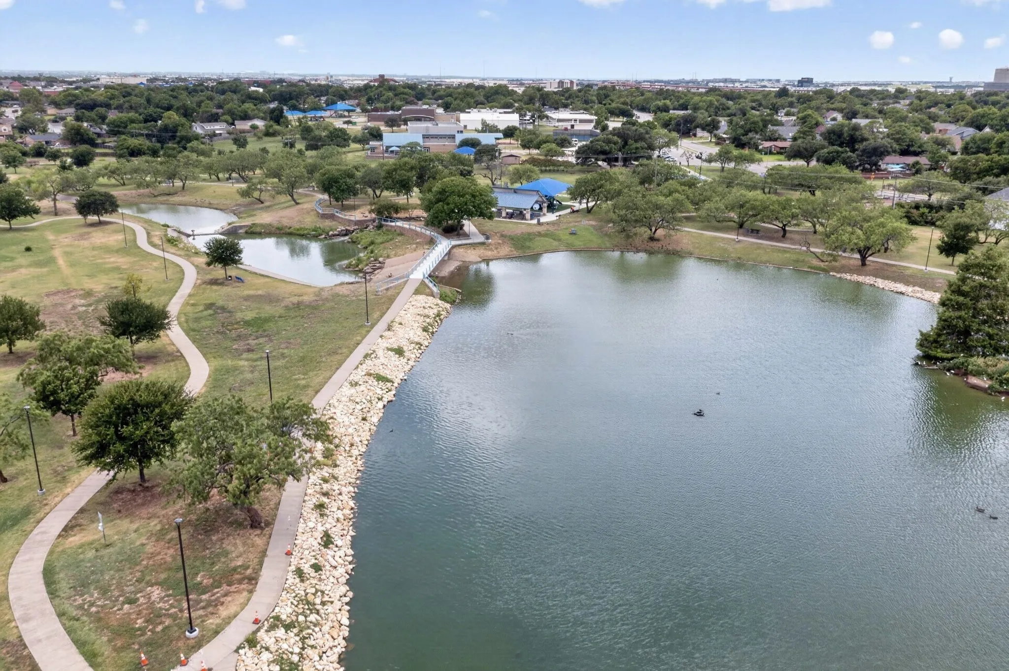 Expansive body of water with a rocky shoreline, bordered by winding pathways and mature trees