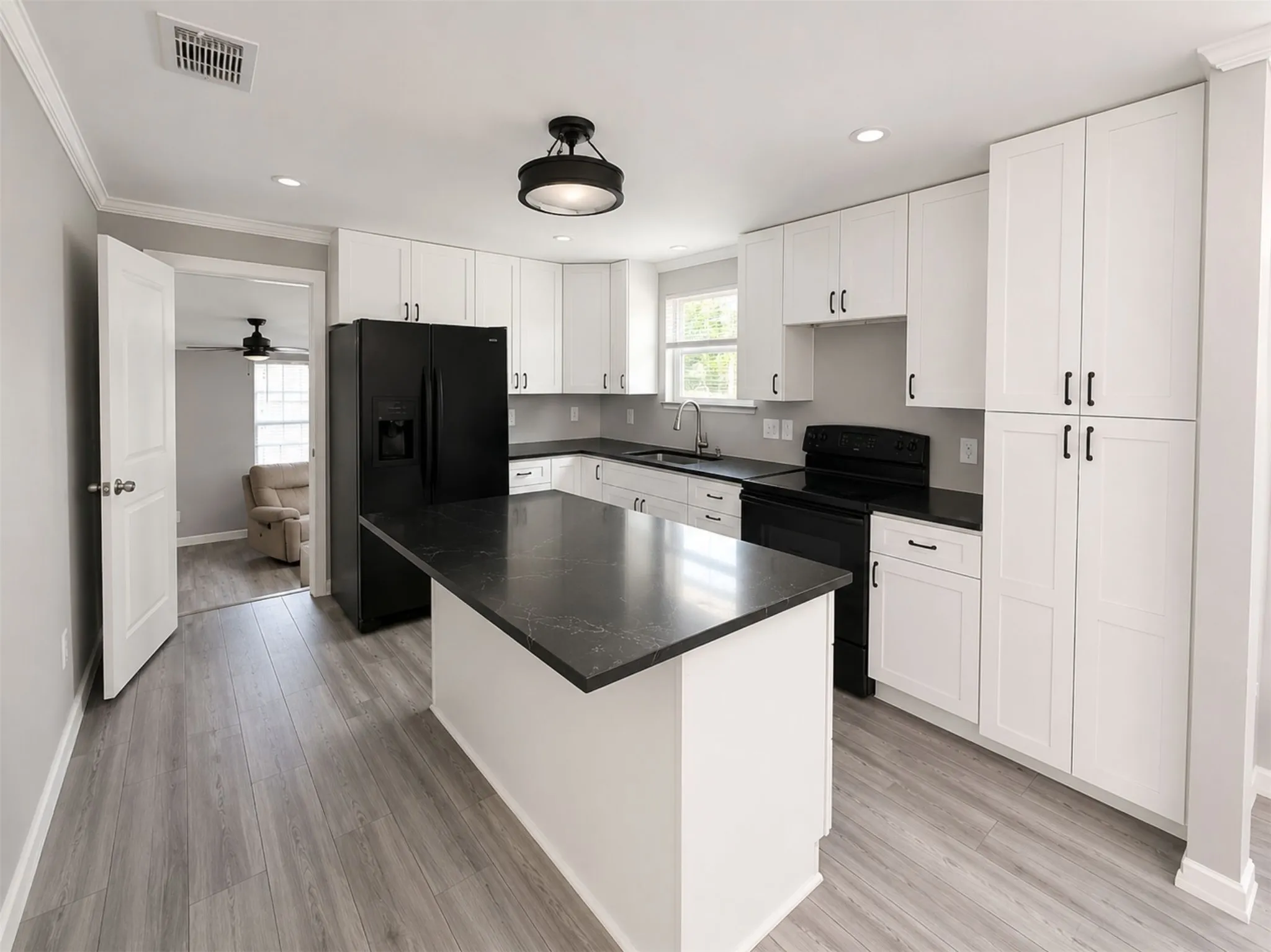 Kitchen featuring white cabinetry, dark countertops, a central island, stainless steel sink, and wood-finish flooring