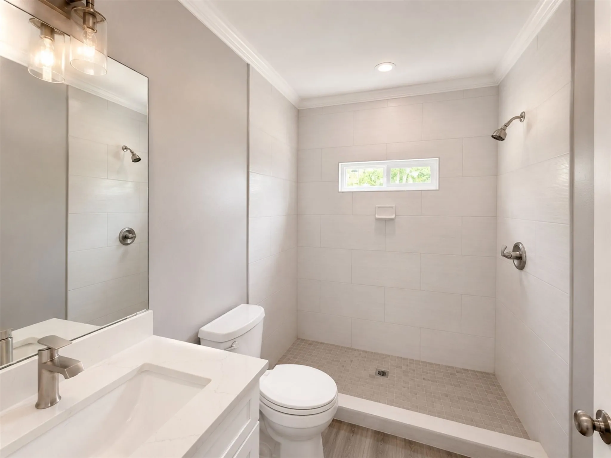 Walk-in shower with tiled walls and floor, vanity with integrated sink and brushed nickel faucet, wall-mounted light fixture, and crown molding