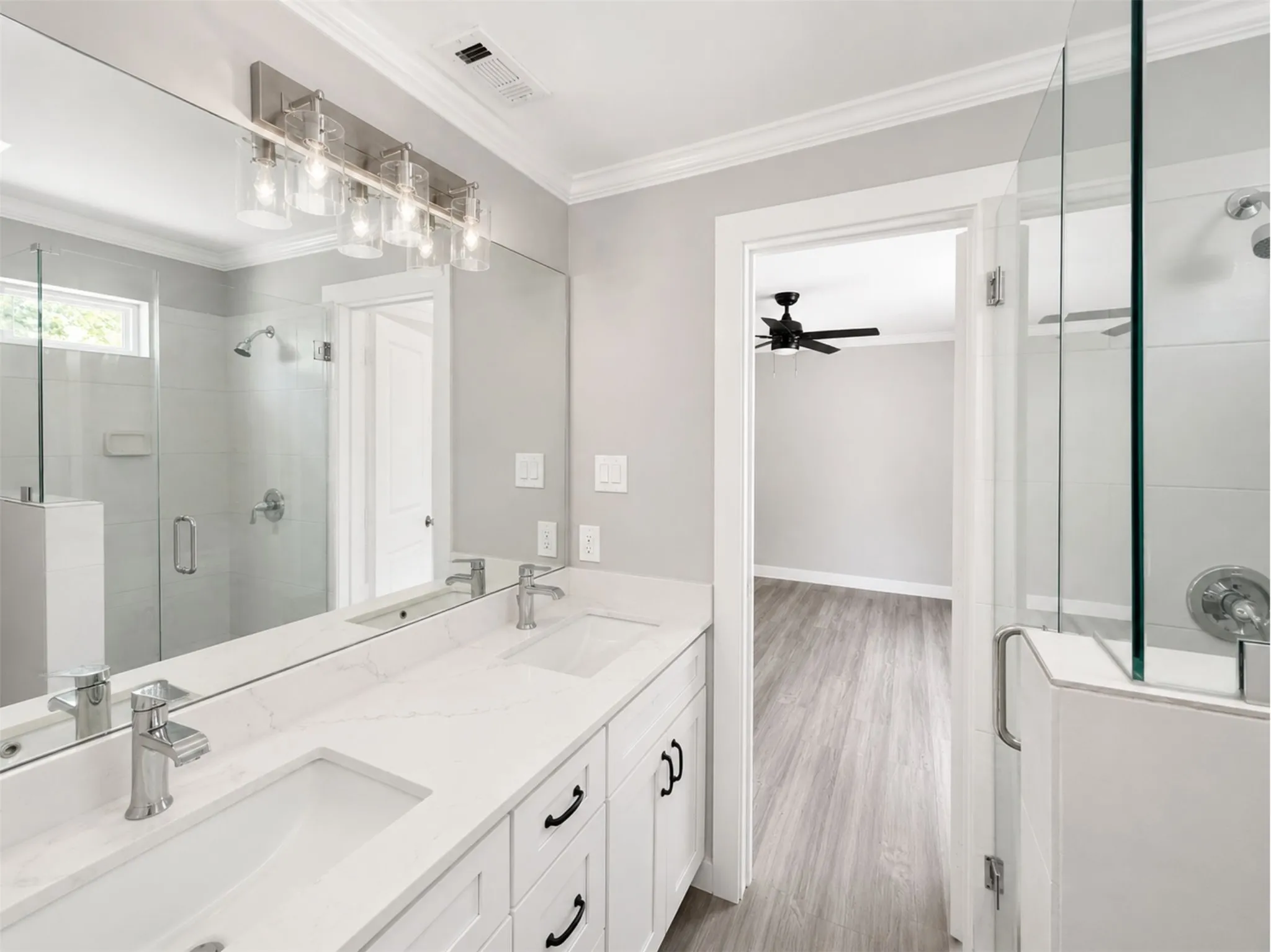 Dual vanity with integrated sinks and chrome faucets, full-width mirror, and glass-enclosed shower